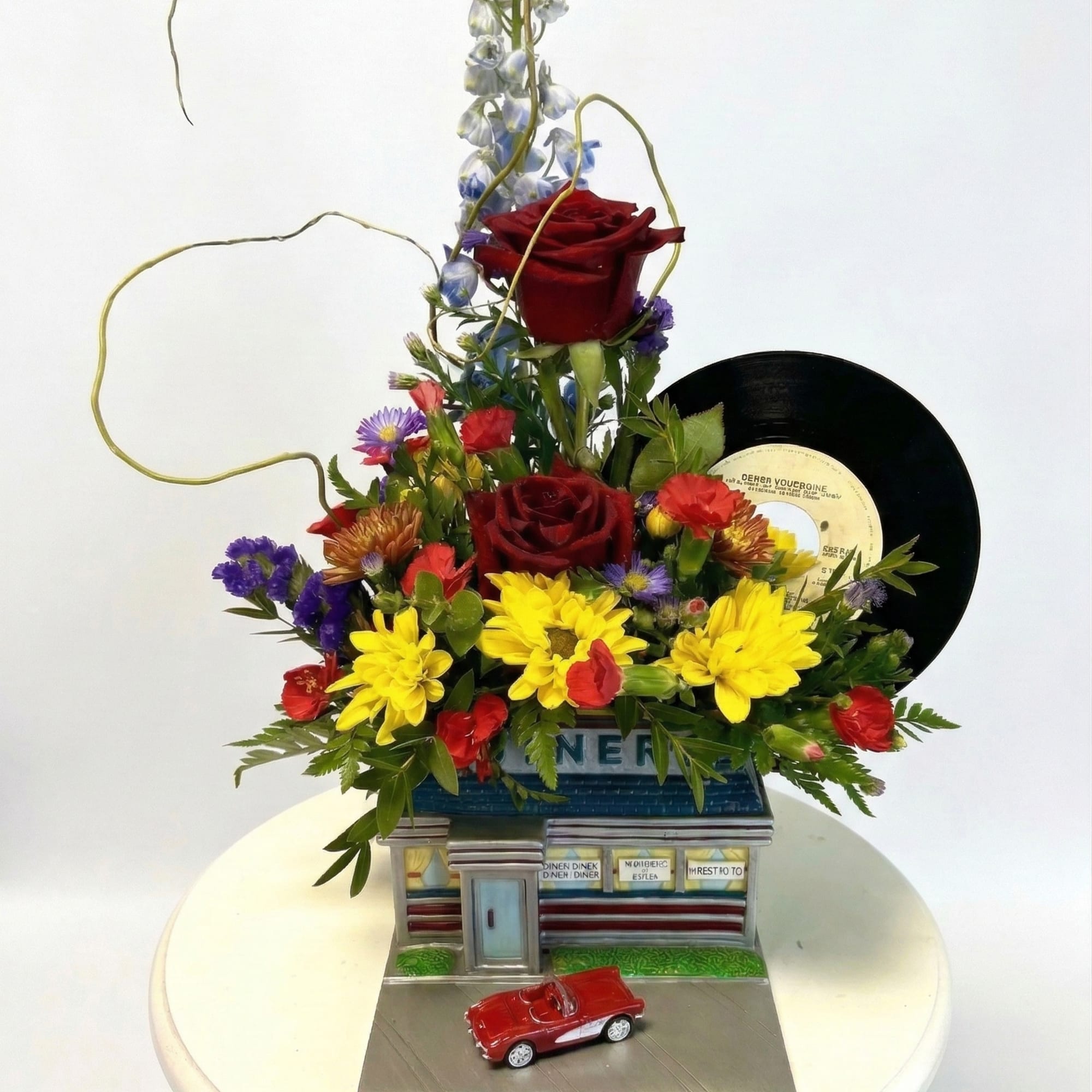 Mixed flower arrangement with roses, daisies, and a vinyl record on a decorative base