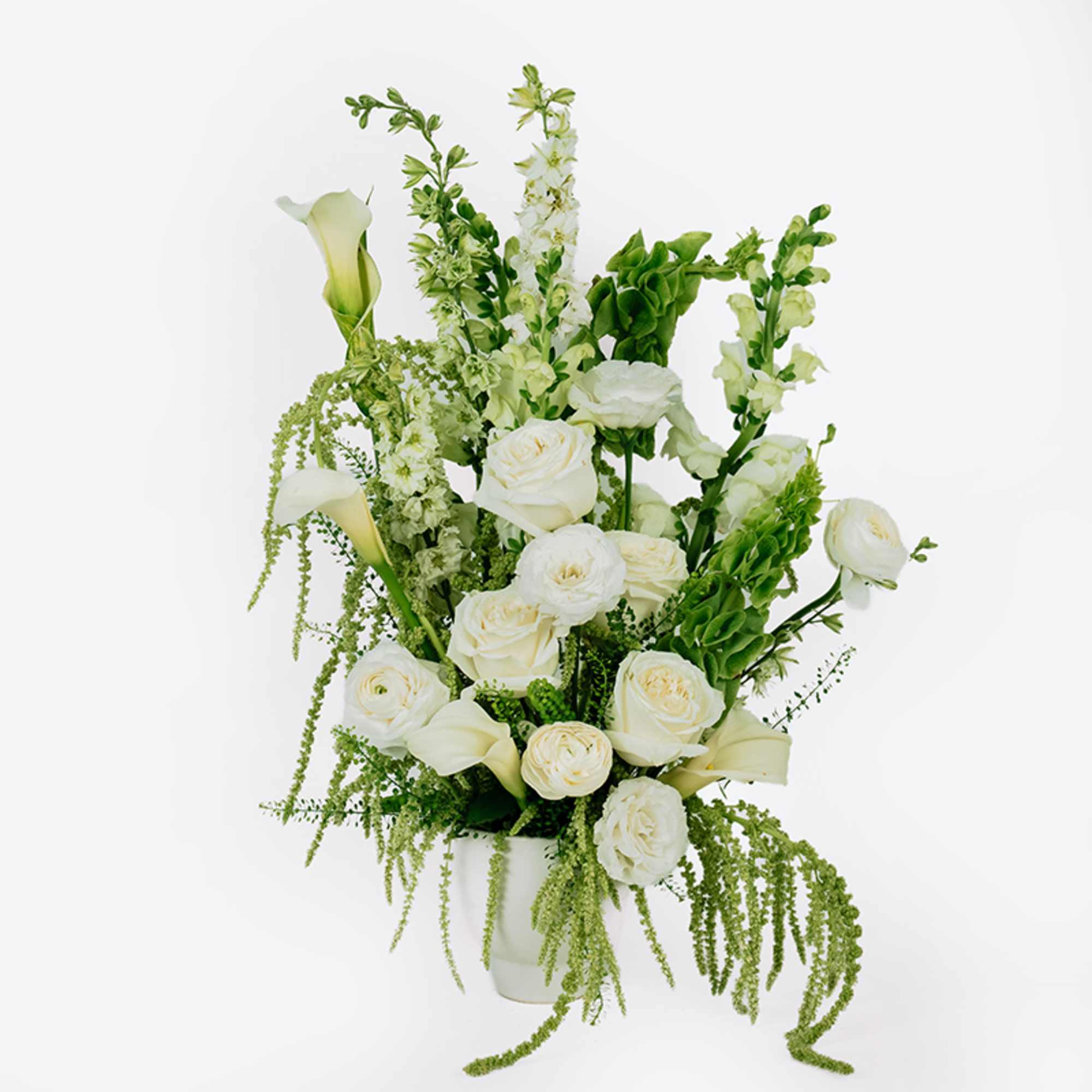 White roses and calla lilies arranged in a white vase with green accents.