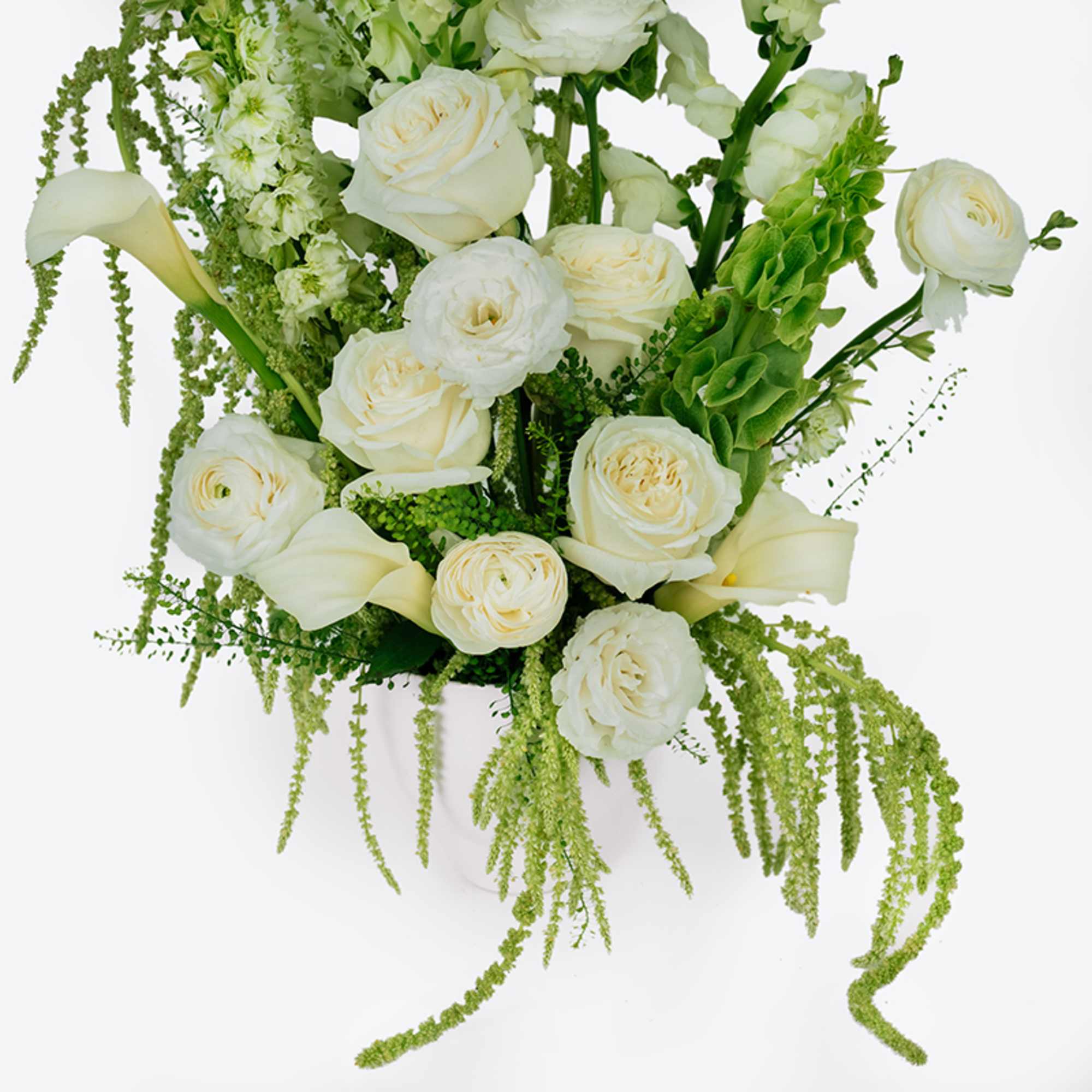 White roses and calla lilies in a white vase with trailing green accents