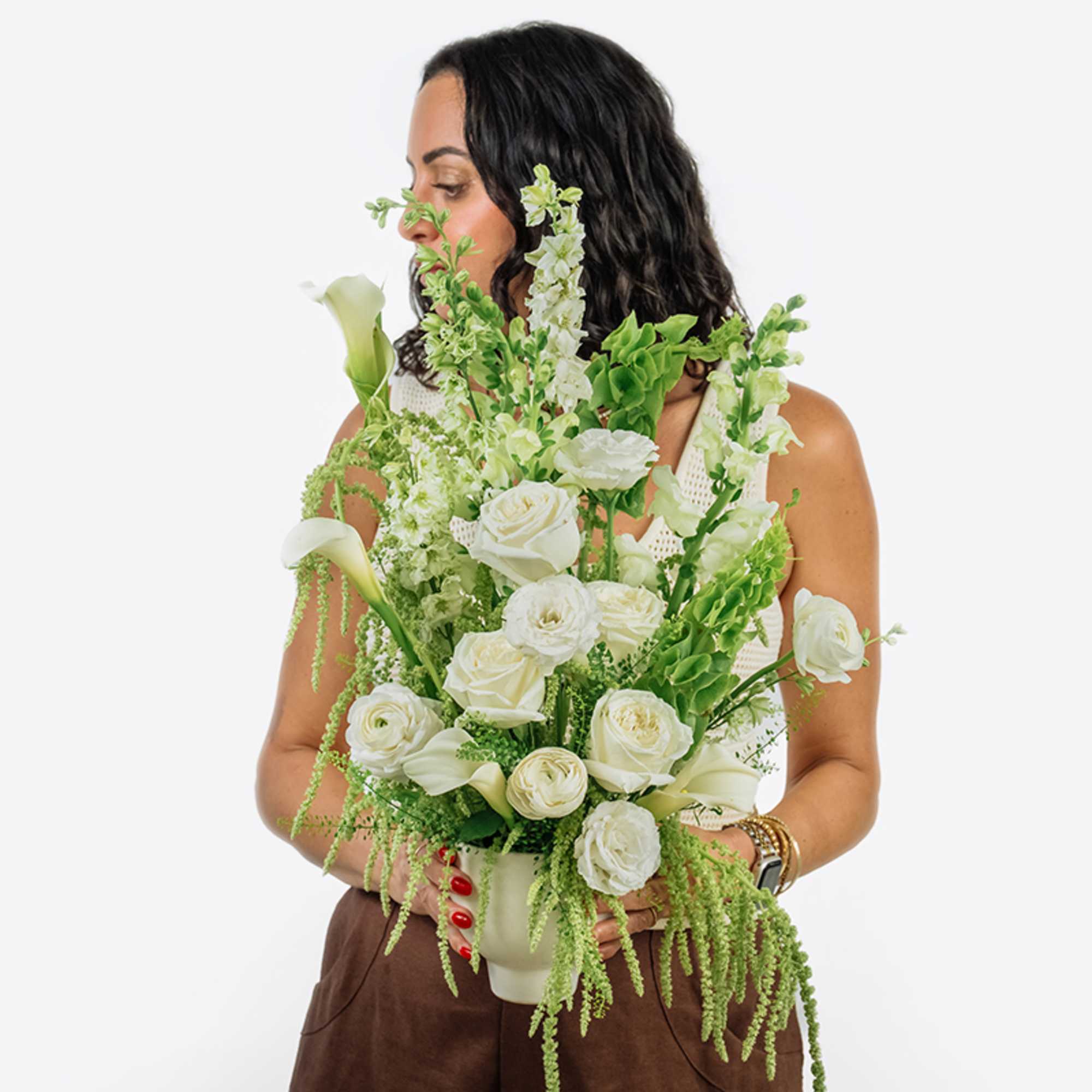 Woman holding a white and green floral arrangement in a vase