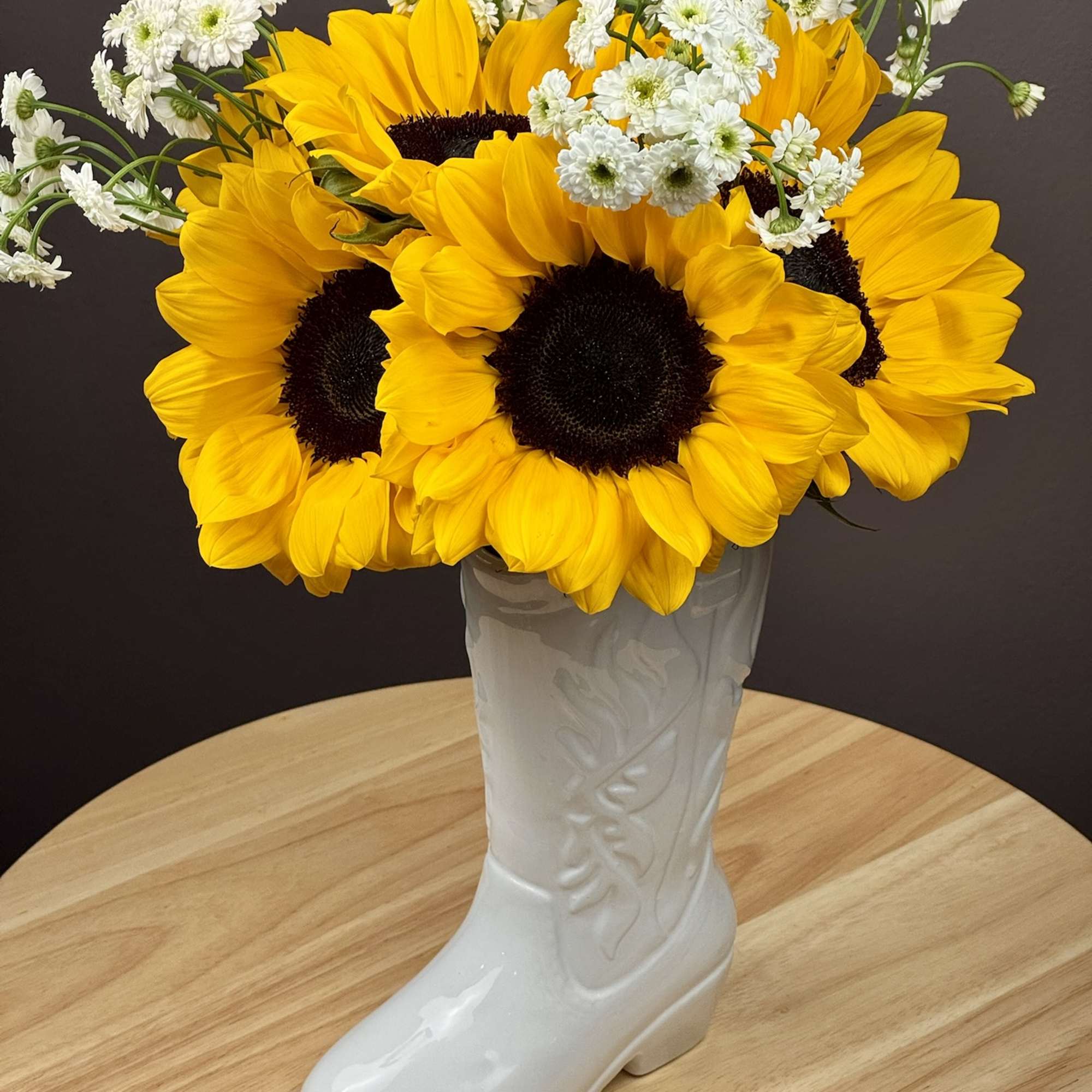 Sunflowers and white daisy-like flowers arranged in a white boot vase