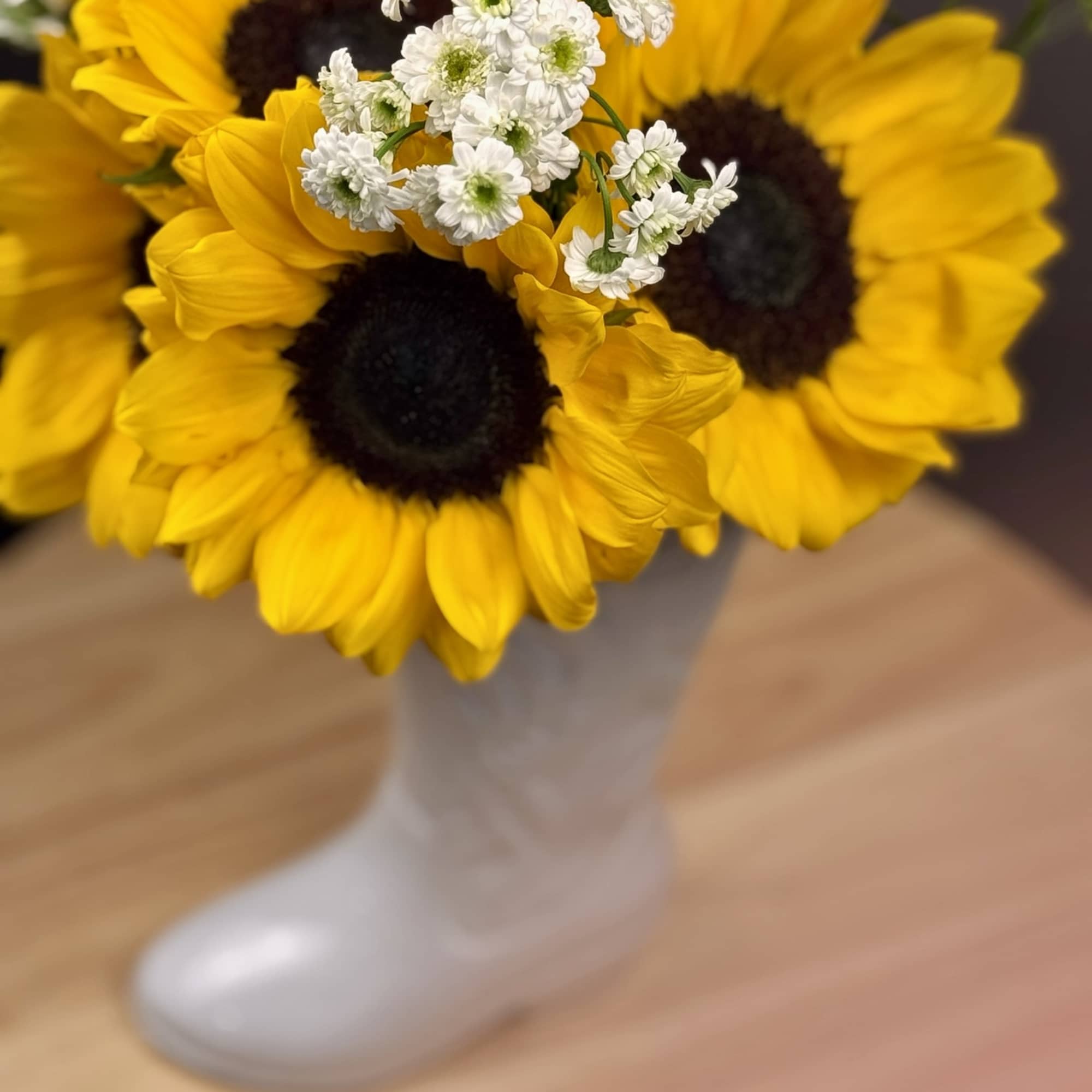 Bouquet of yellow sunflowers with small white filler flowers in a white boot vase