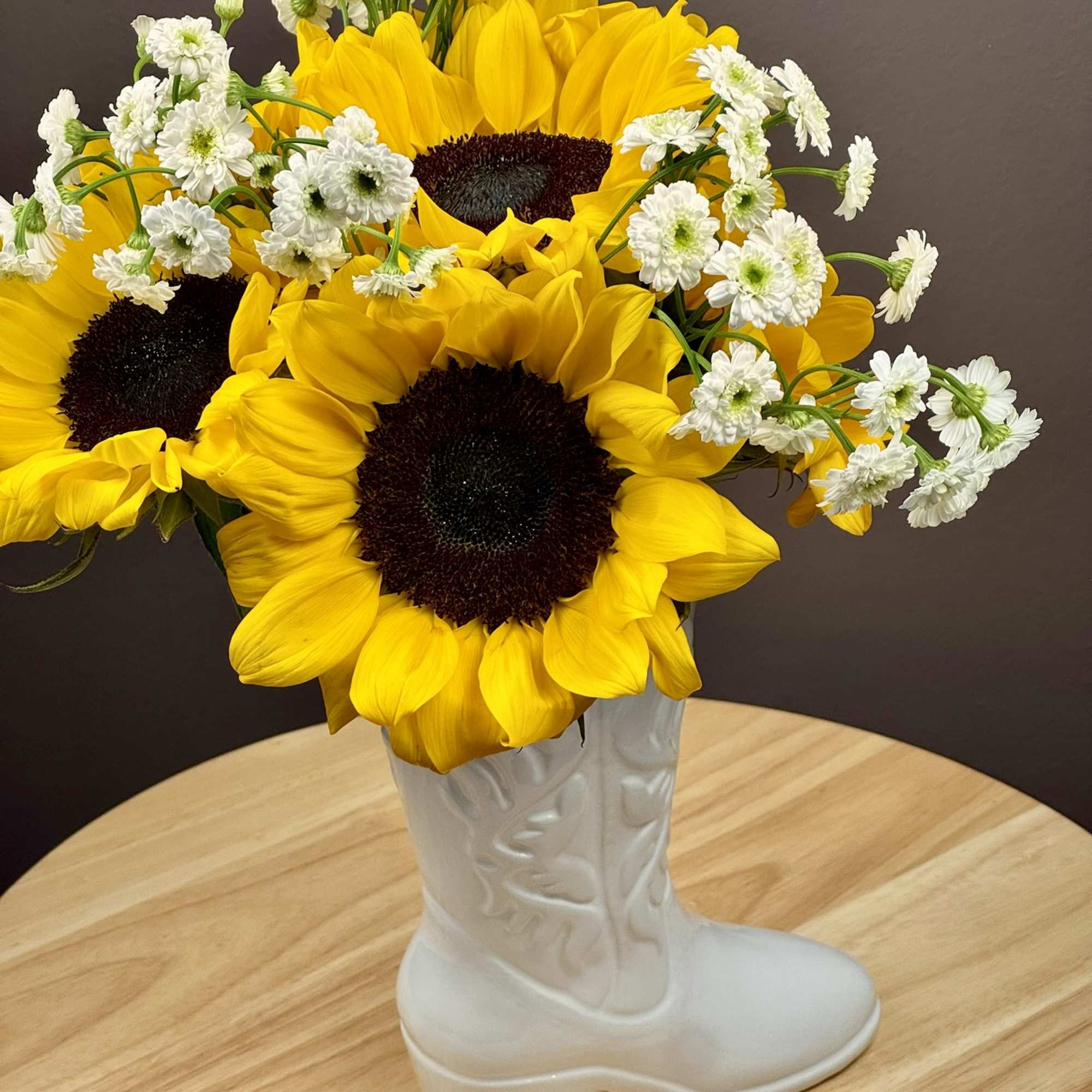 Sunflowers and white daisies arranged in a white boot-shaped vase