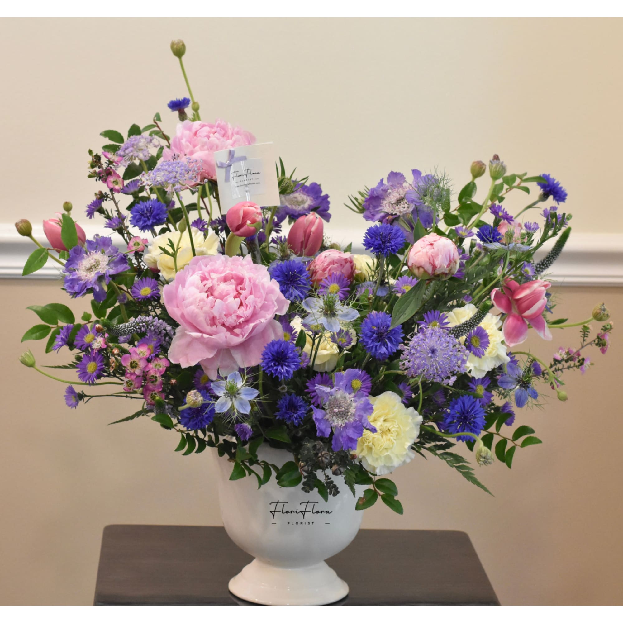 Large mixed bouquet in a white pedestal vase with pink and purple flowers