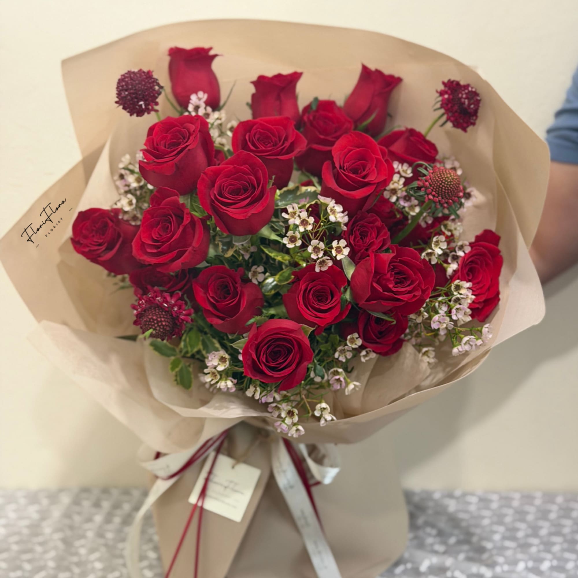 Bouquet of red roses with small white filler flowers in tan wrapping