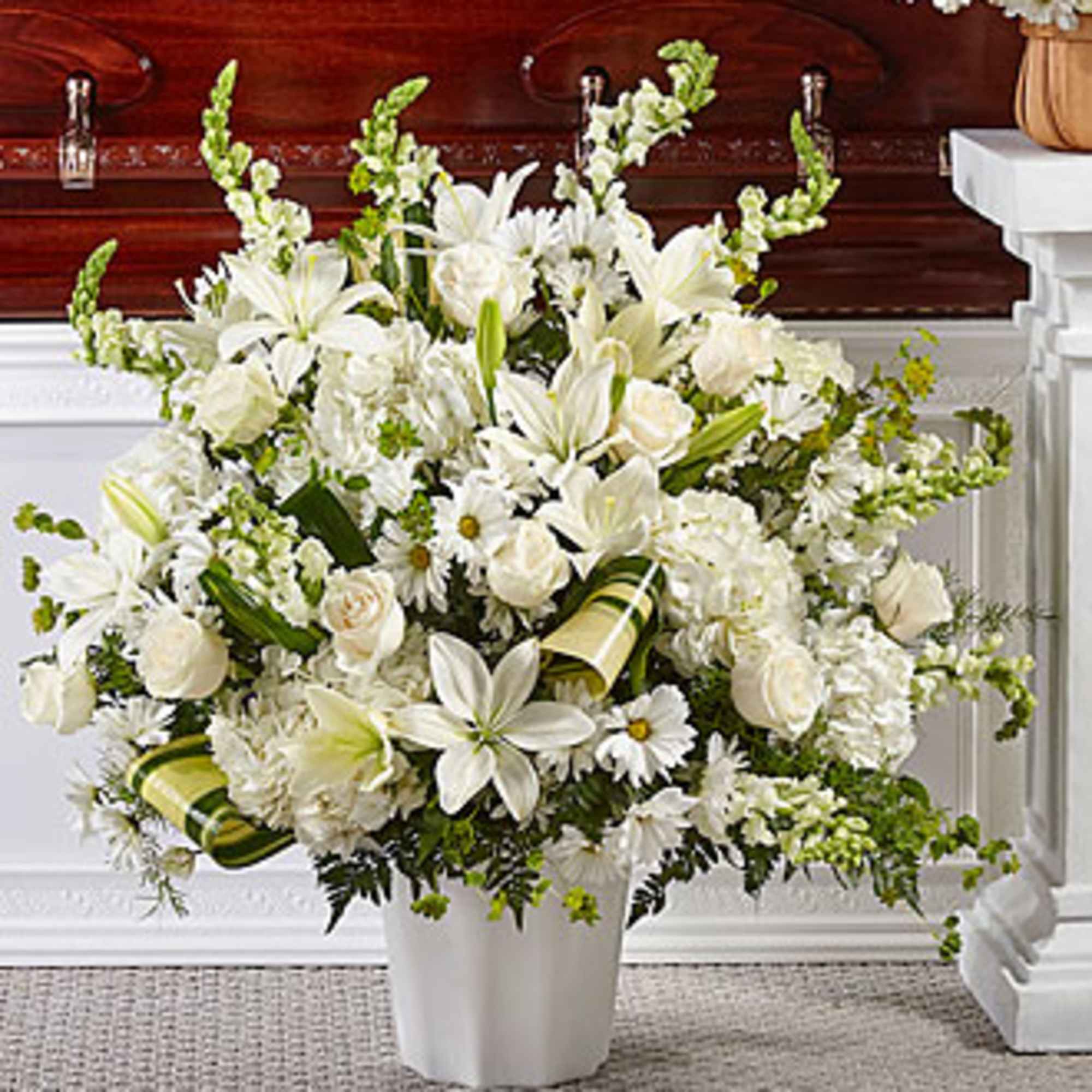 White funeral spray with lilies, roses, and daisies in a white urn