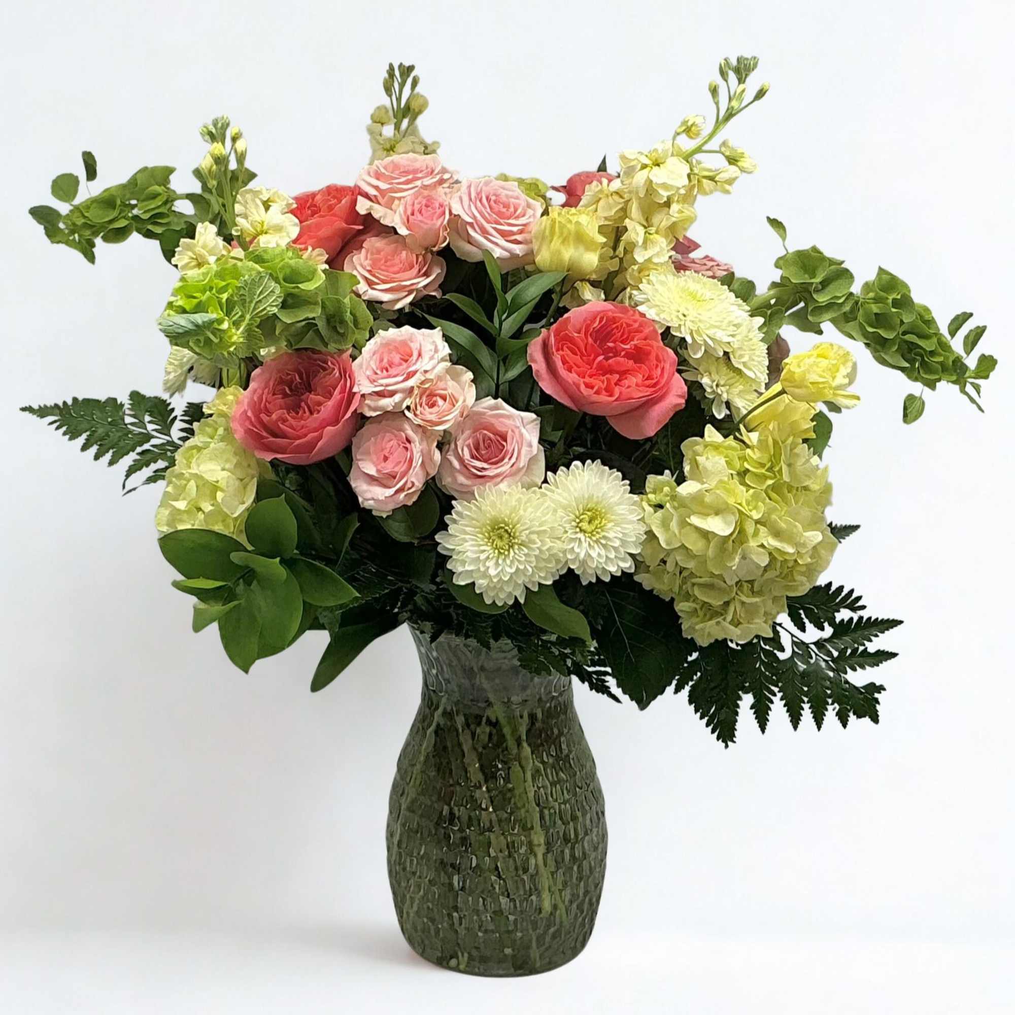 Bouquet of pink roses, white mums, and pale yellow hydrangeas in a textured vase
