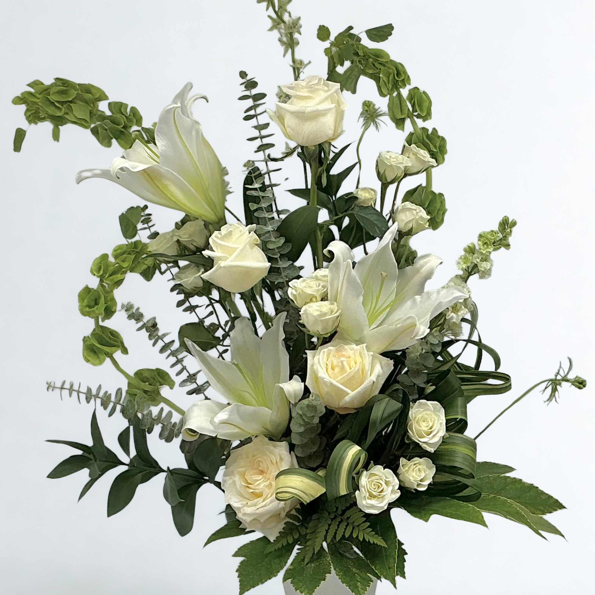 White lilies and roses arranged in a vase with green foliage