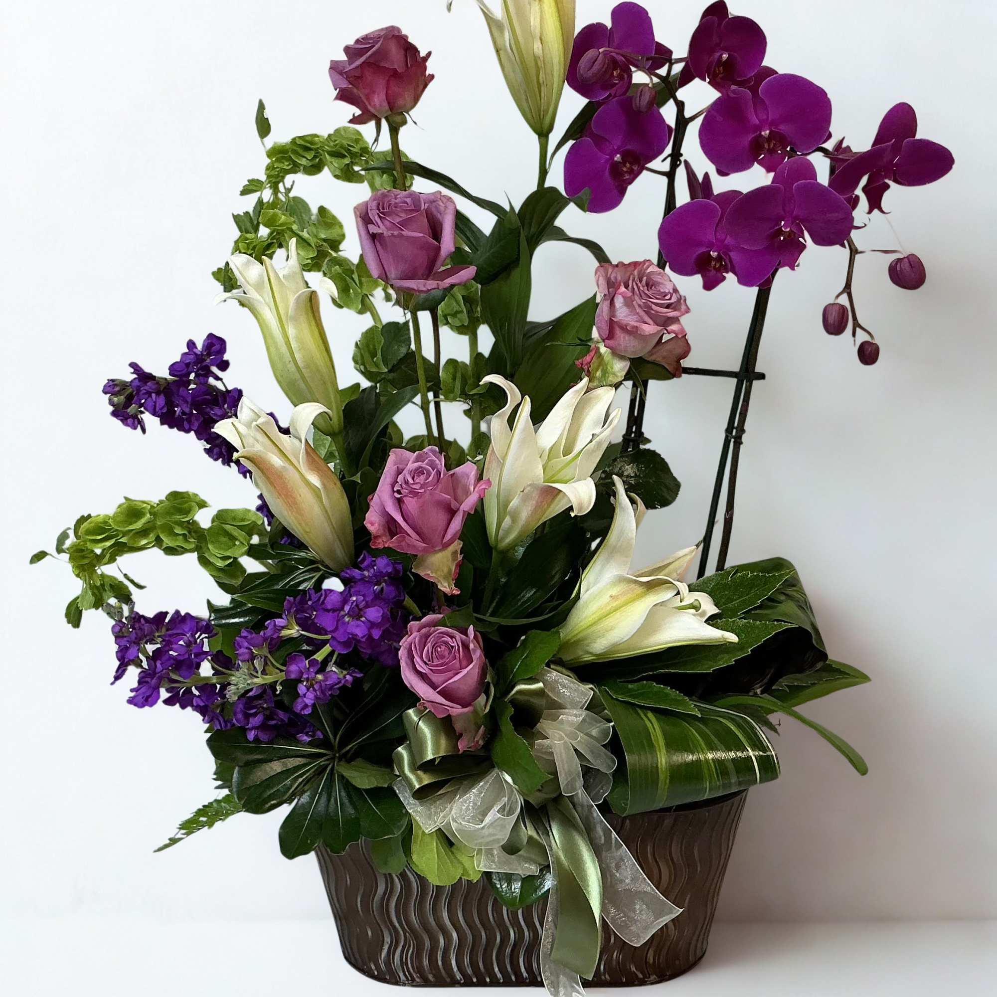 Purple roses and white lilies with orchids in a decorative vase