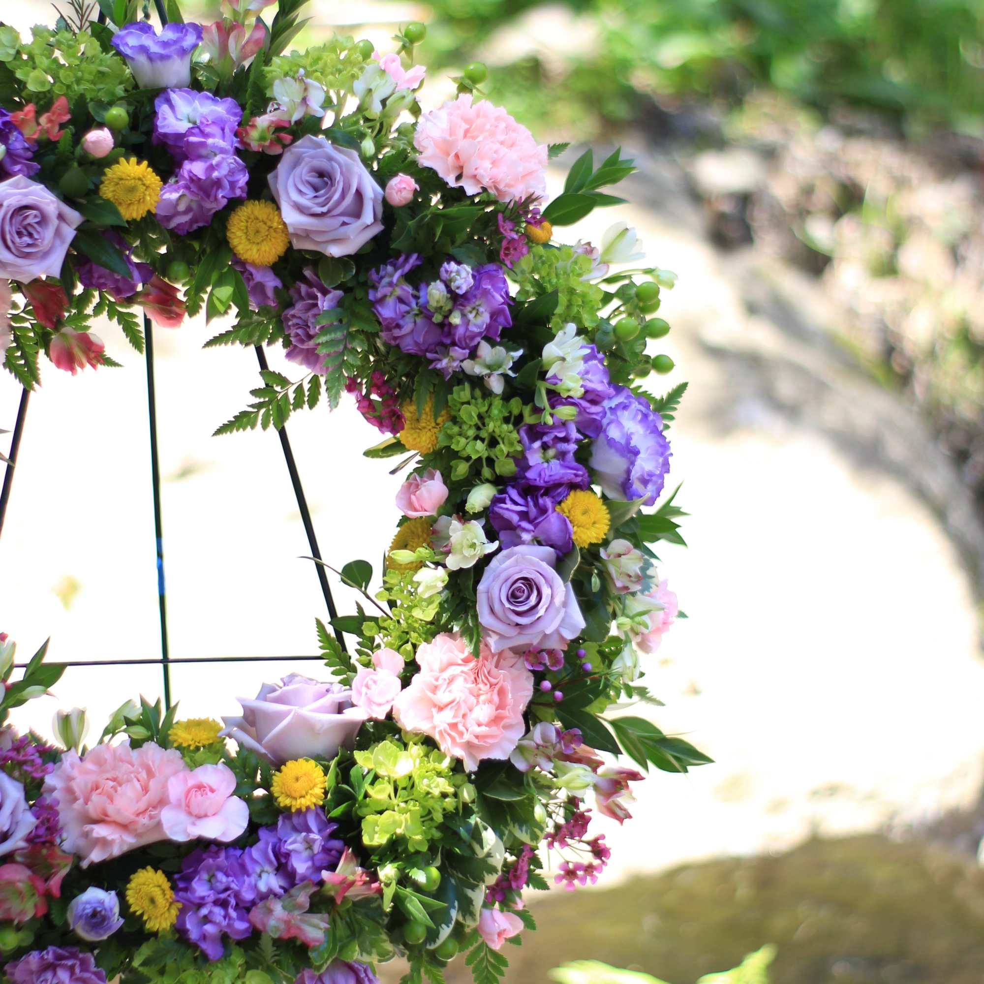 Floral wreath with purple, pink, and yellow blooms on a metal stand
