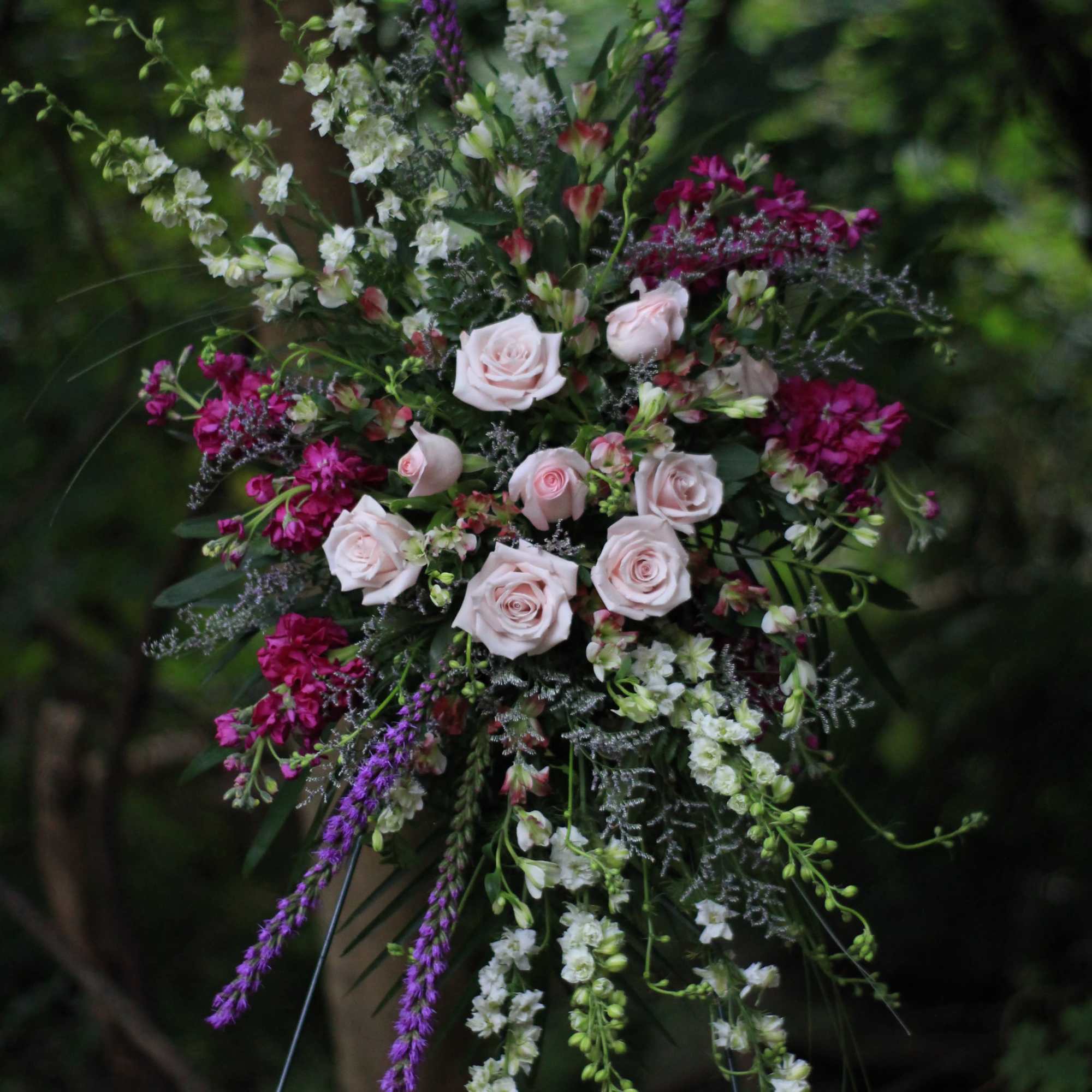 Tall floral spray with pale pink roses and purple and white blooms on a stand