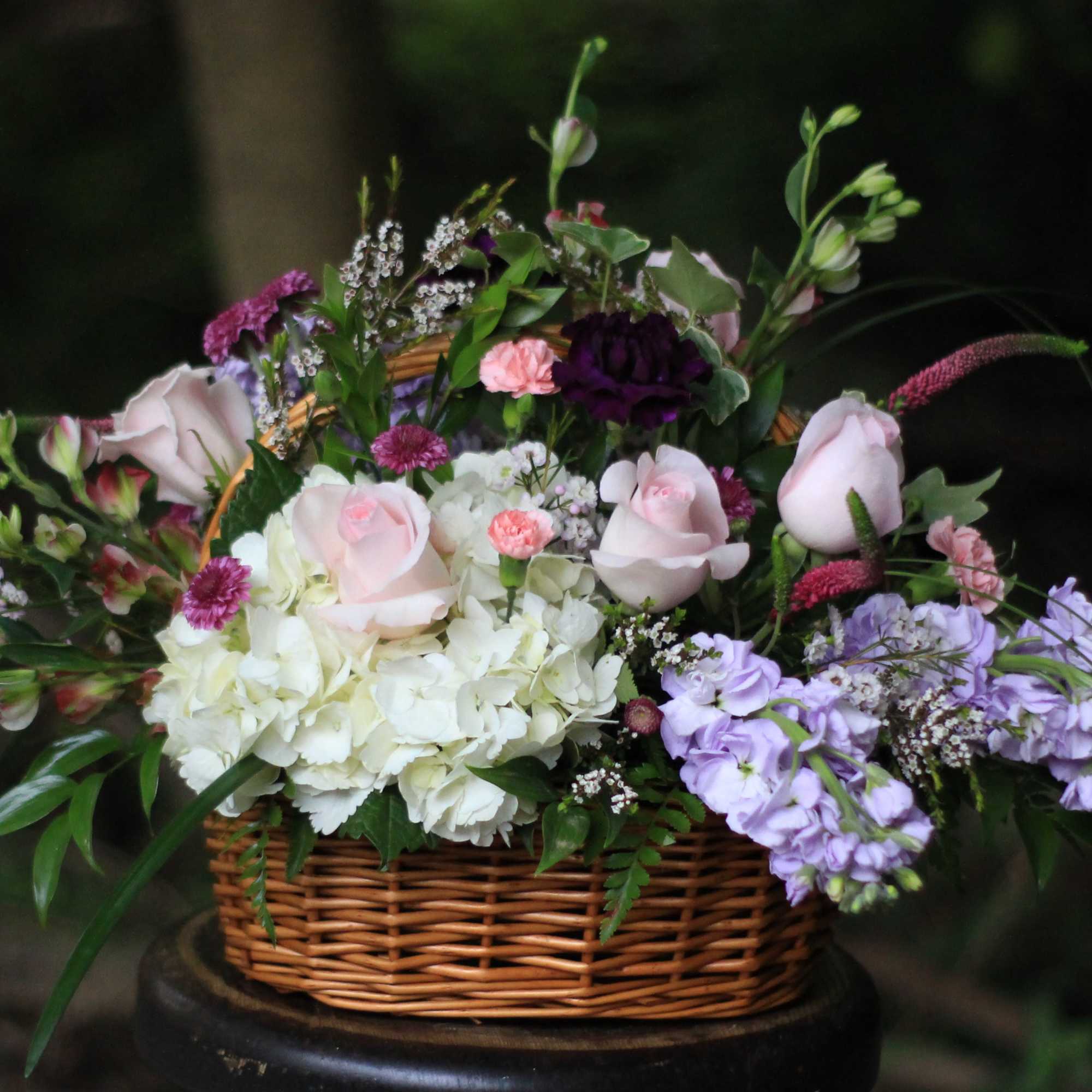 Basket arrangement of pastel roses, hydrangeas, and purple flowers