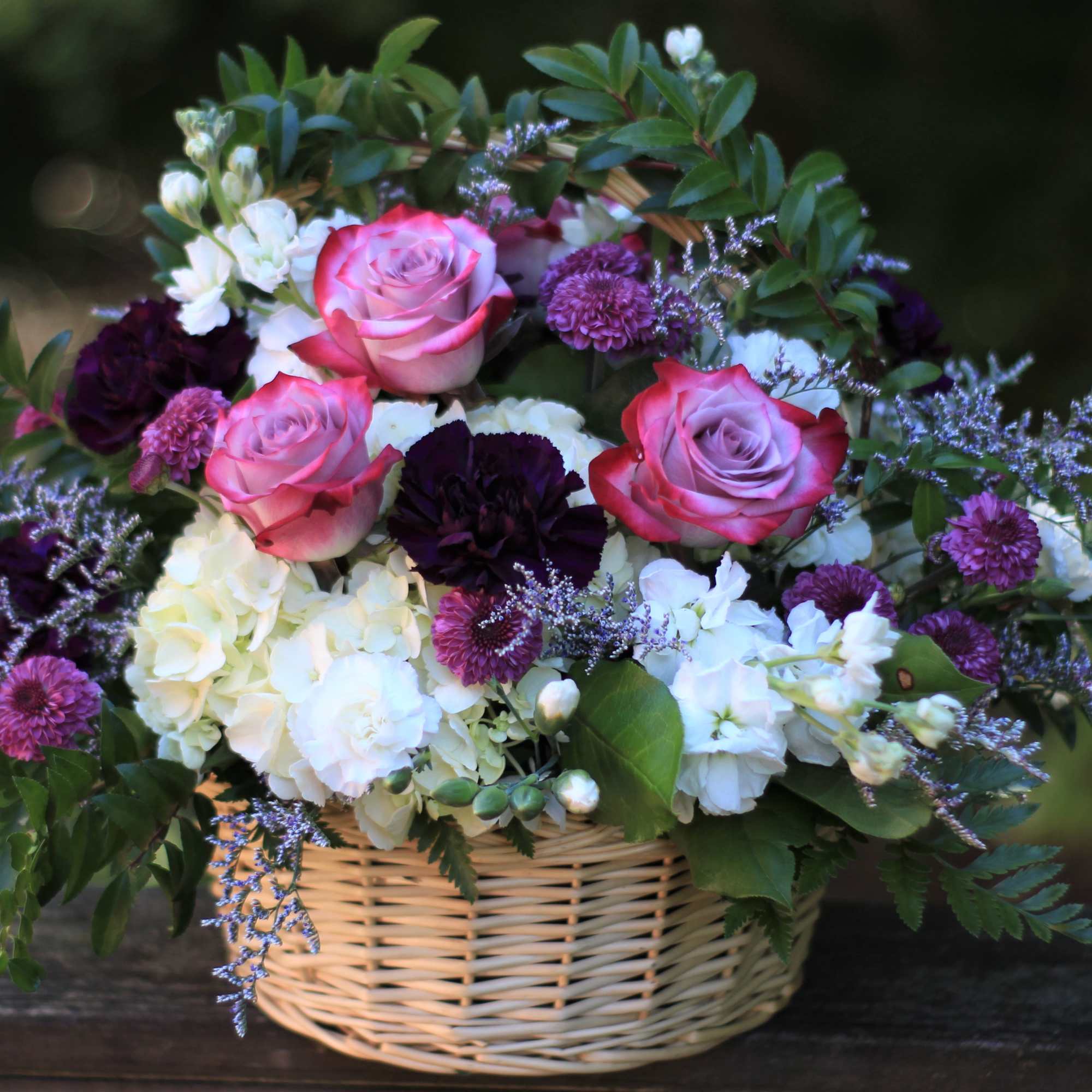 Basket arrangement of pink roses, white hydrangeas, and purple flowers