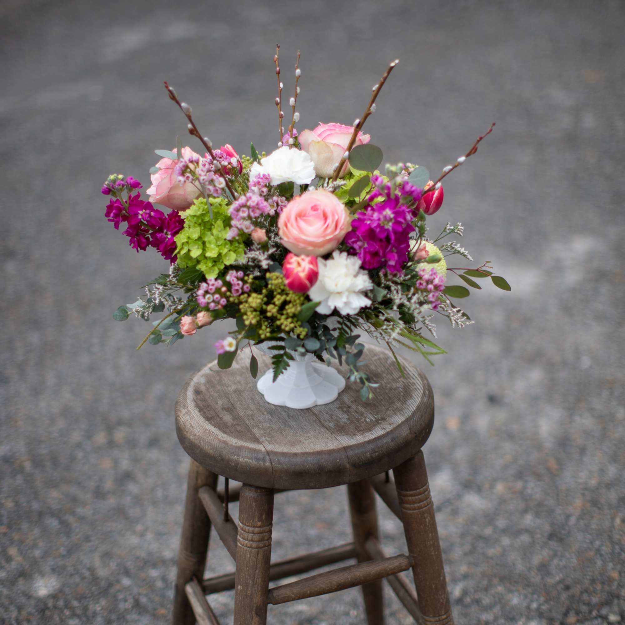 Pink and white floral arrangement in a white vase on a wooden stool