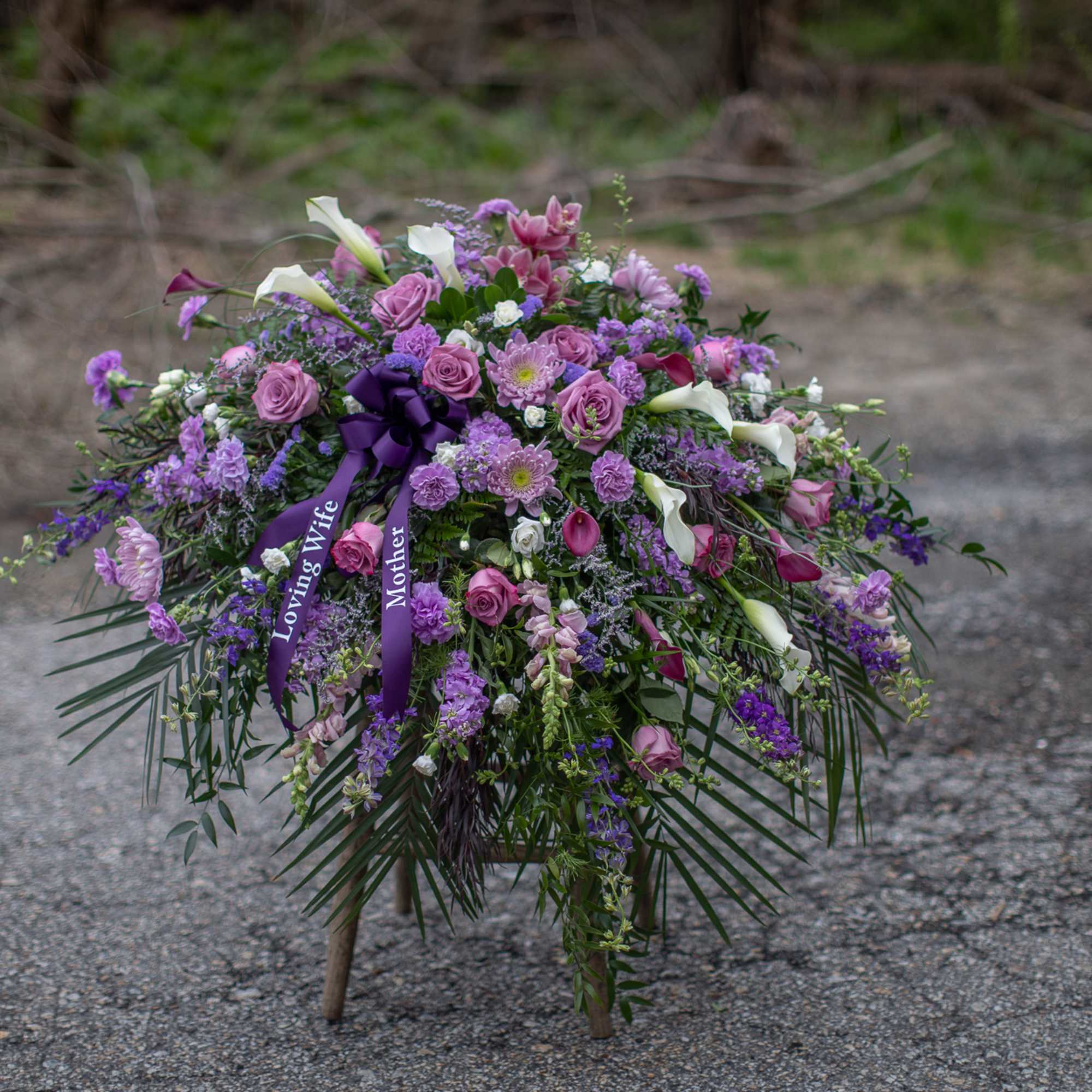 Large purple and white floral spray with ribbon on a stand