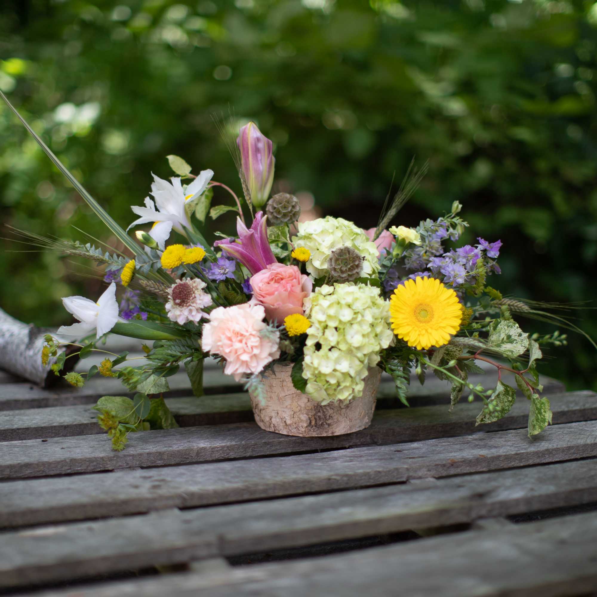 Mixed bouquet in a low textured container with pink, yellow, white, and purple flowers