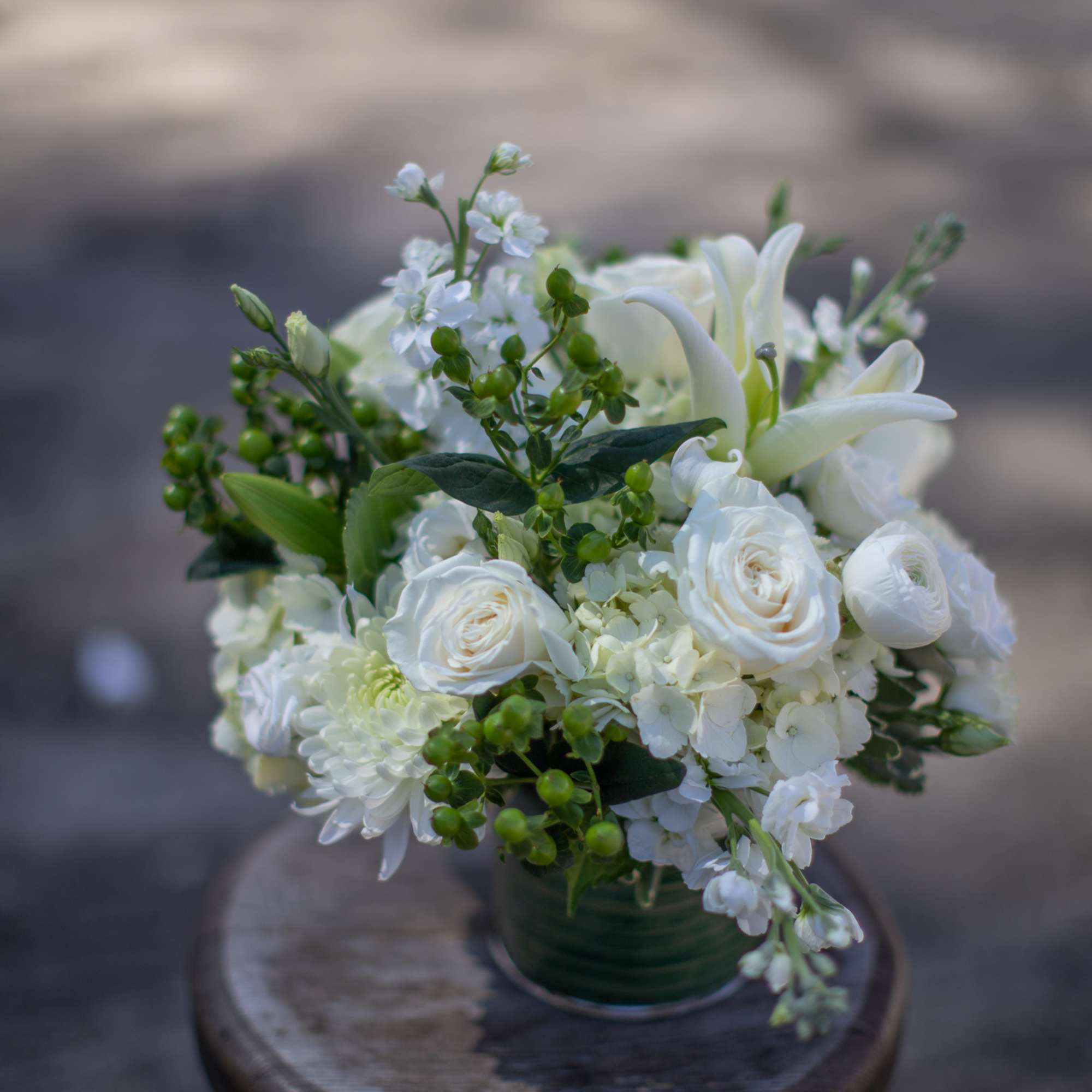 White floral arrangement in a green vase with roses and lilies