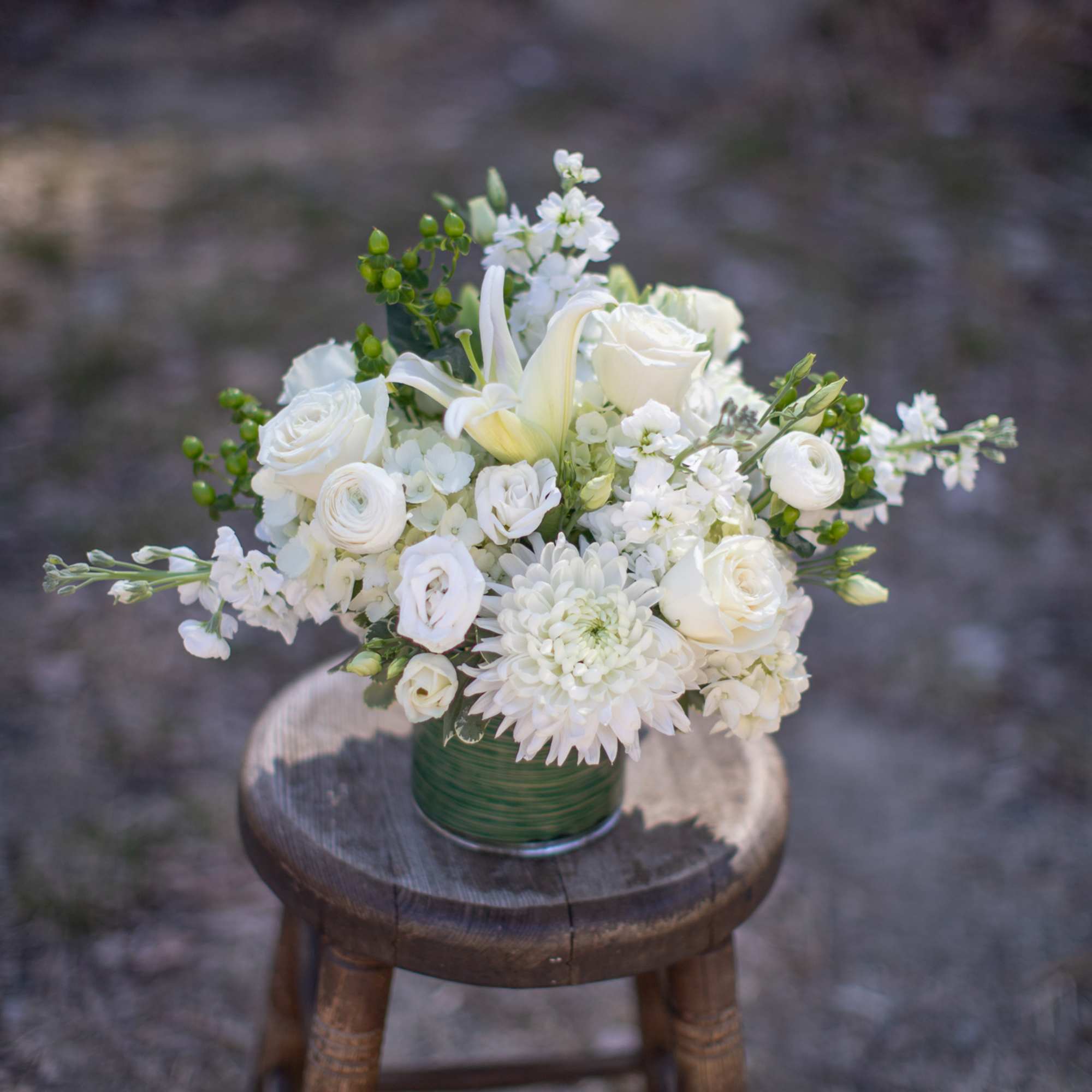 White floral arrangement in a green vase on a wooden stool