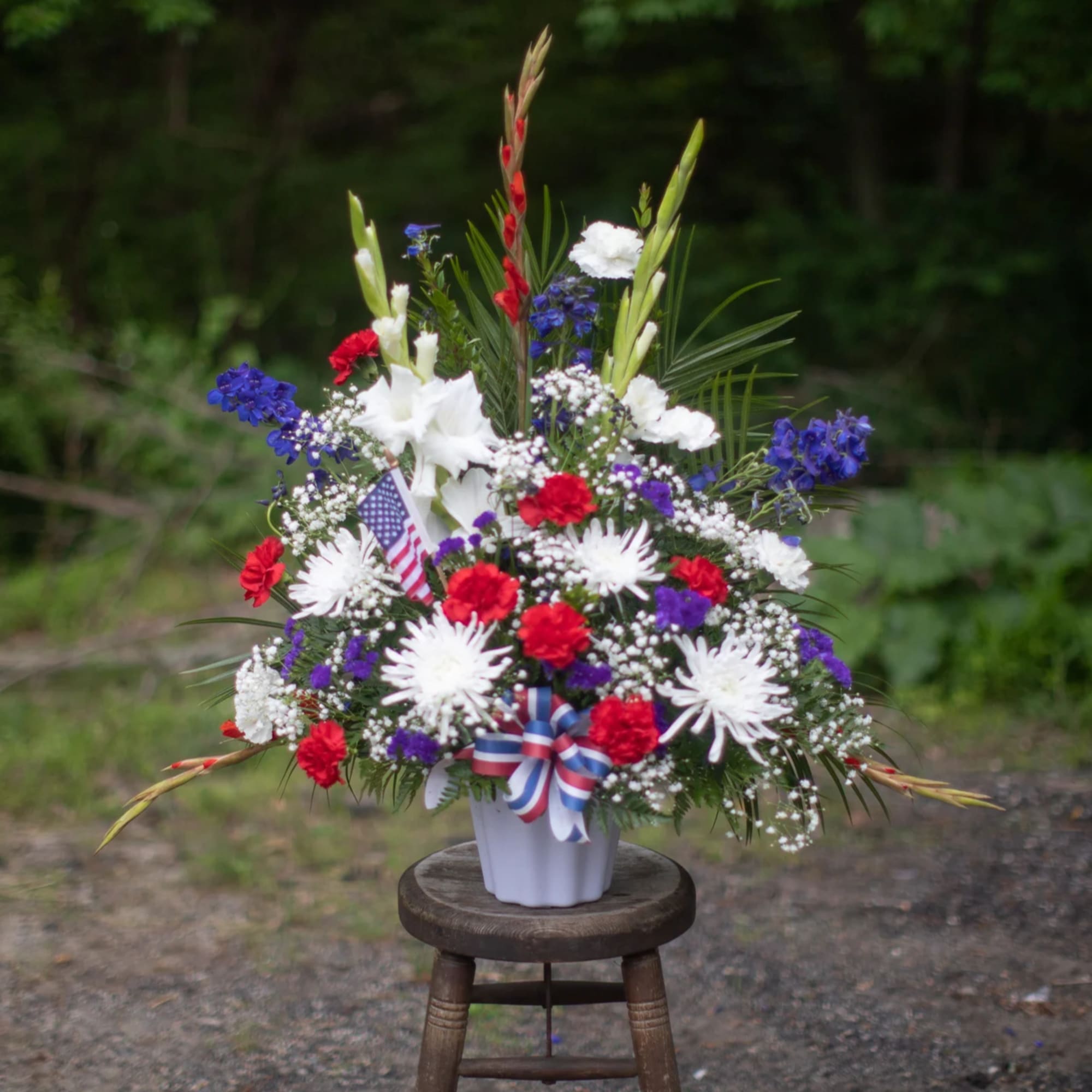 Red, white, and blue floral arrangement in a white vase with a small flag