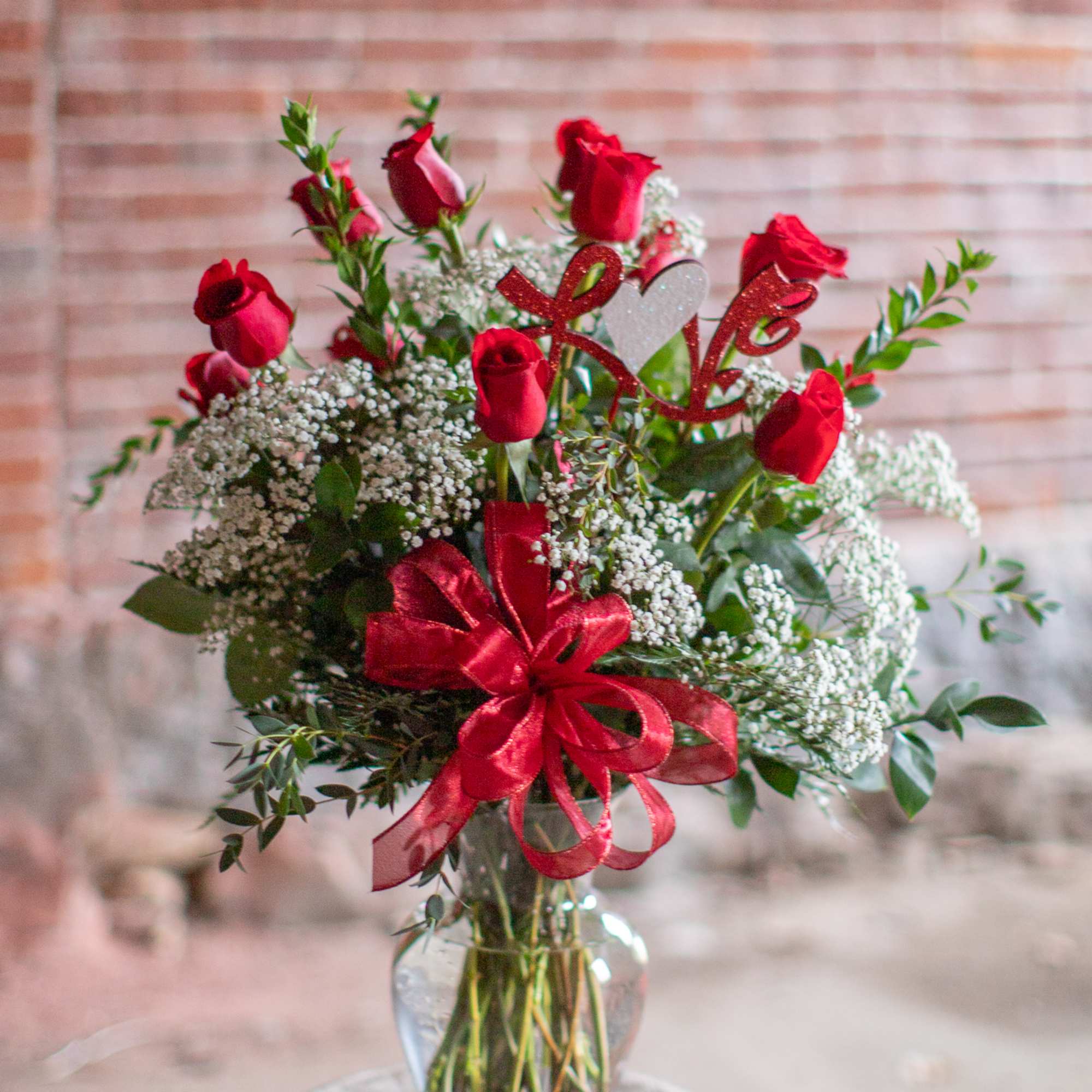 Red roses in a glass vase with baby's breath and a red ribbon bow