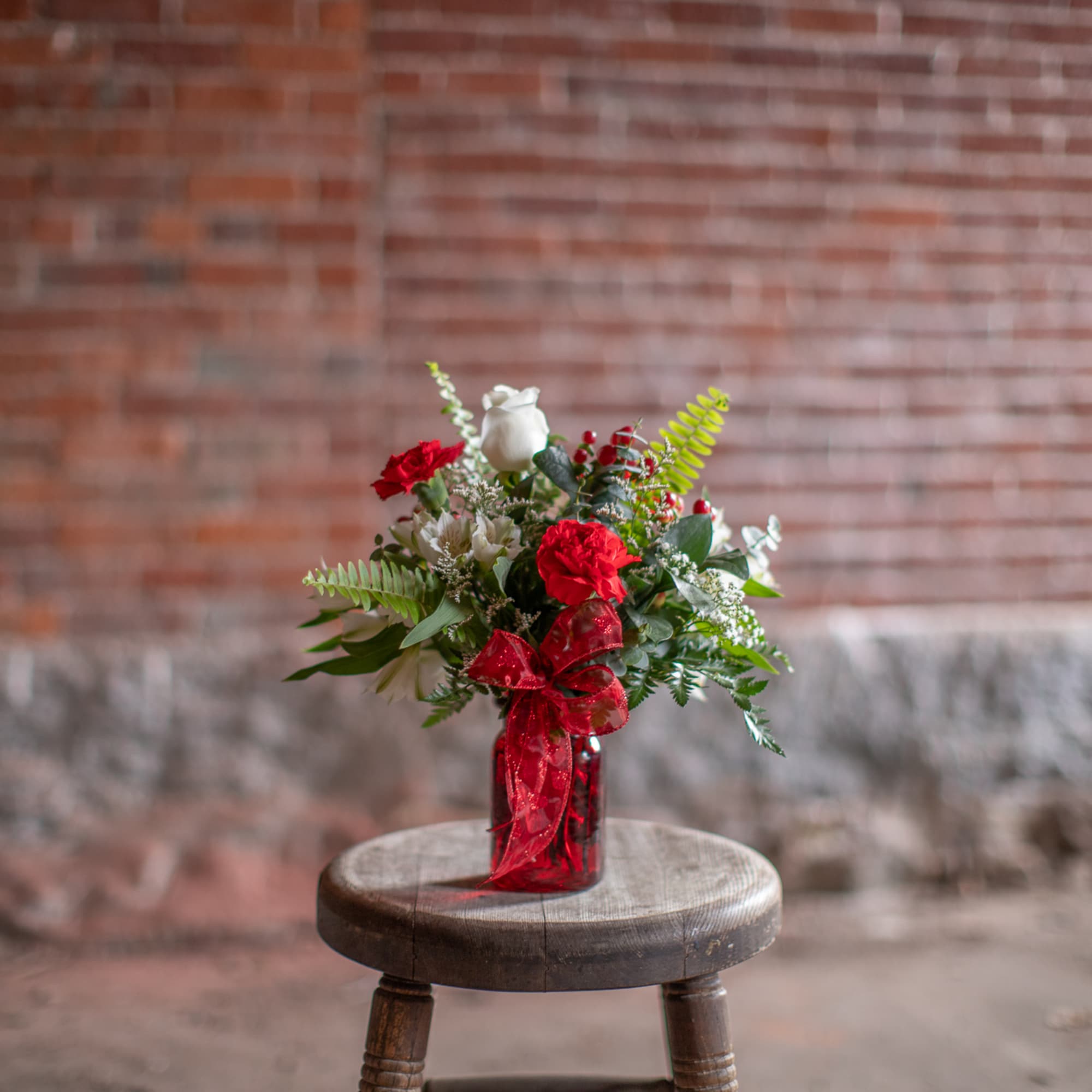 Red and white bouquet in a red glass vase with a ribbon