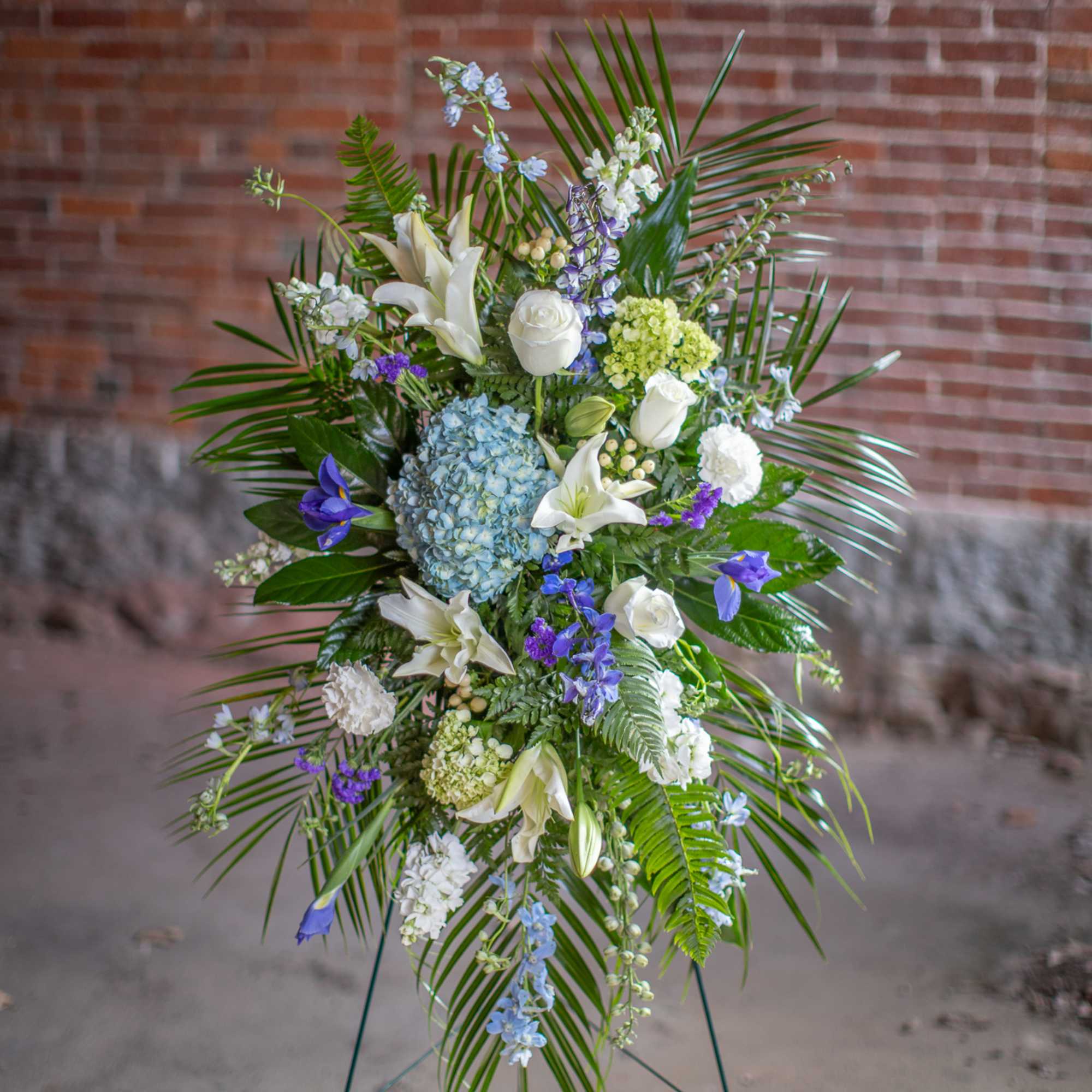 Tall floral standing spray with white lilies, roses, and blue hydrangea