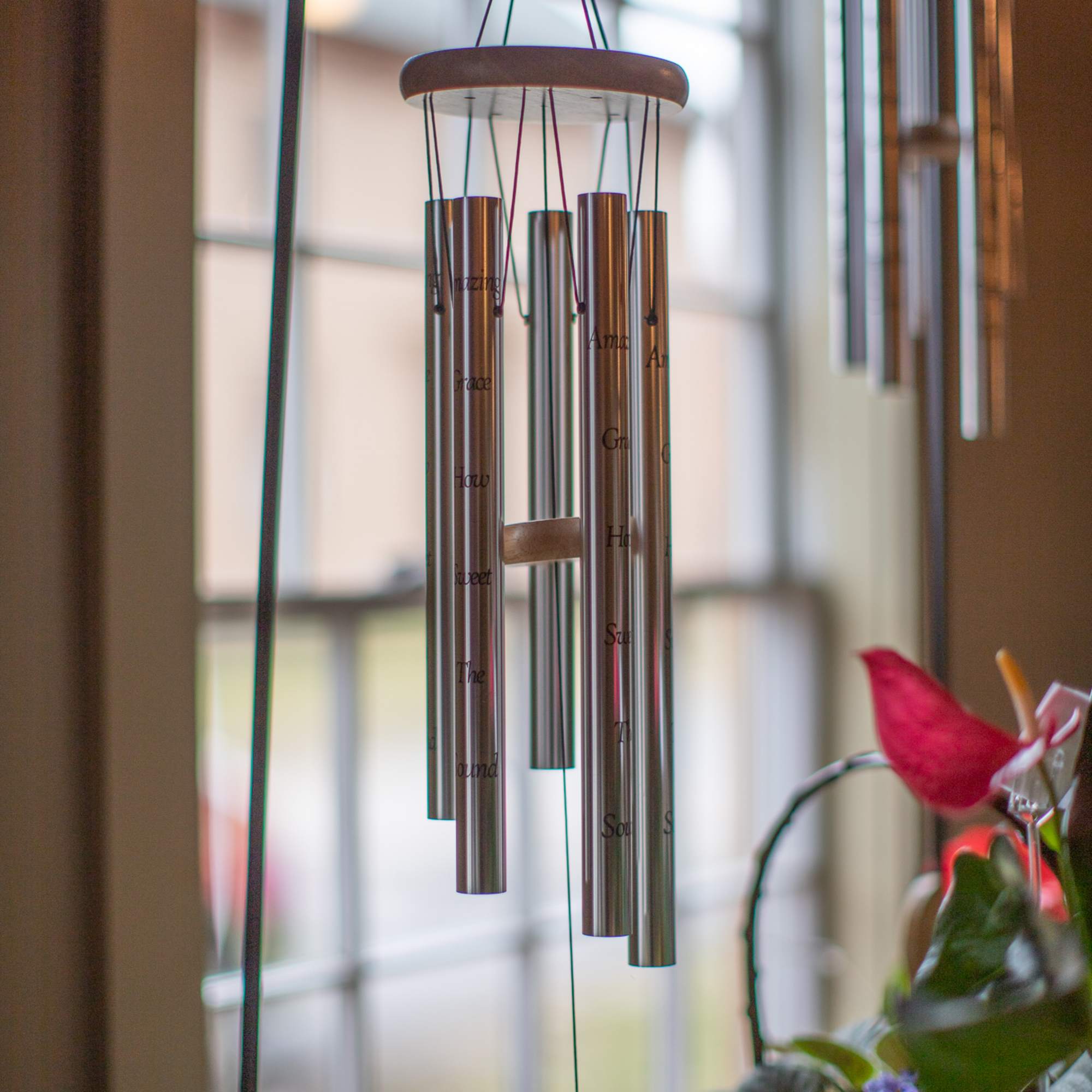 Hanging metal wind chime with engraved tubes near a window