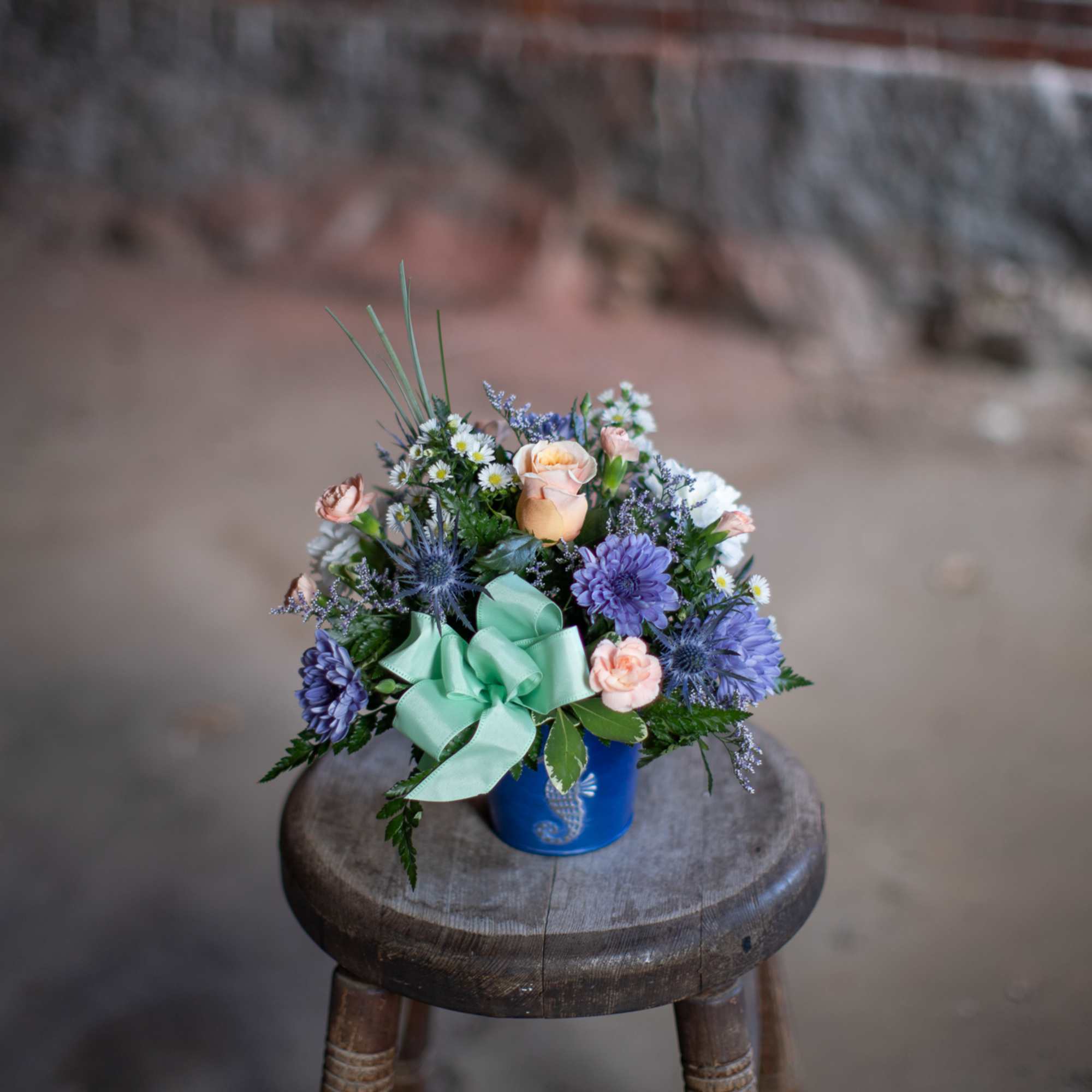 Small mixed flower arrangement in a blue container with a mint ribbon