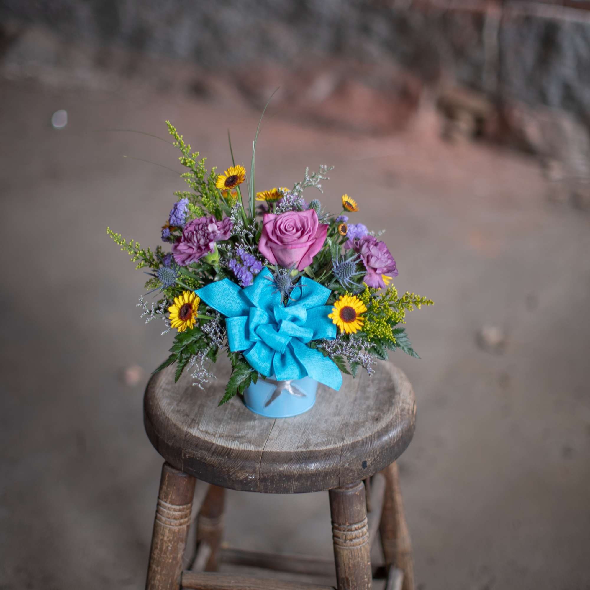 Small mixed flower arrangement in a blue container with a bright ribbon