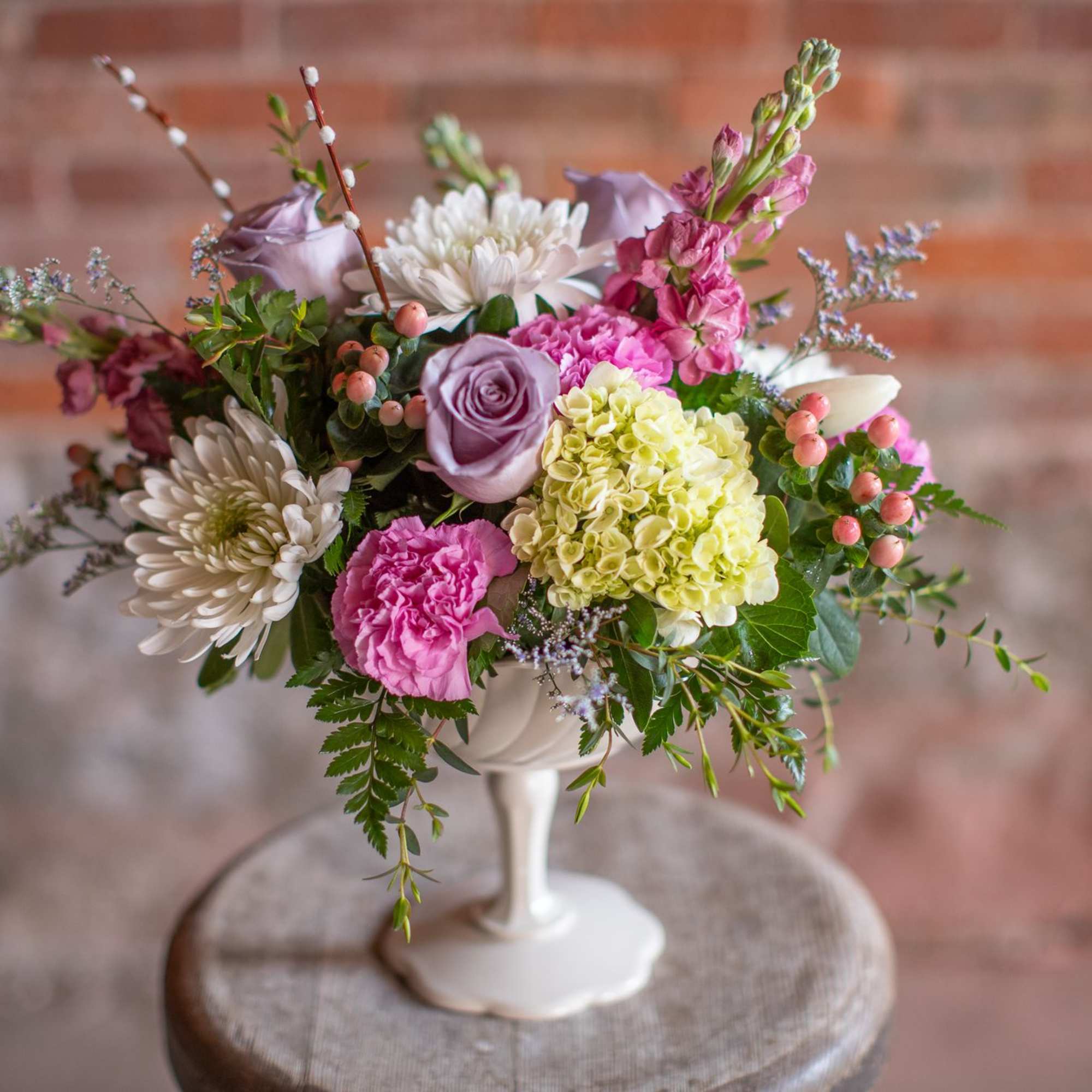 Mixed bouquet in a white pedestal vase with pink, lavender, and white blooms
