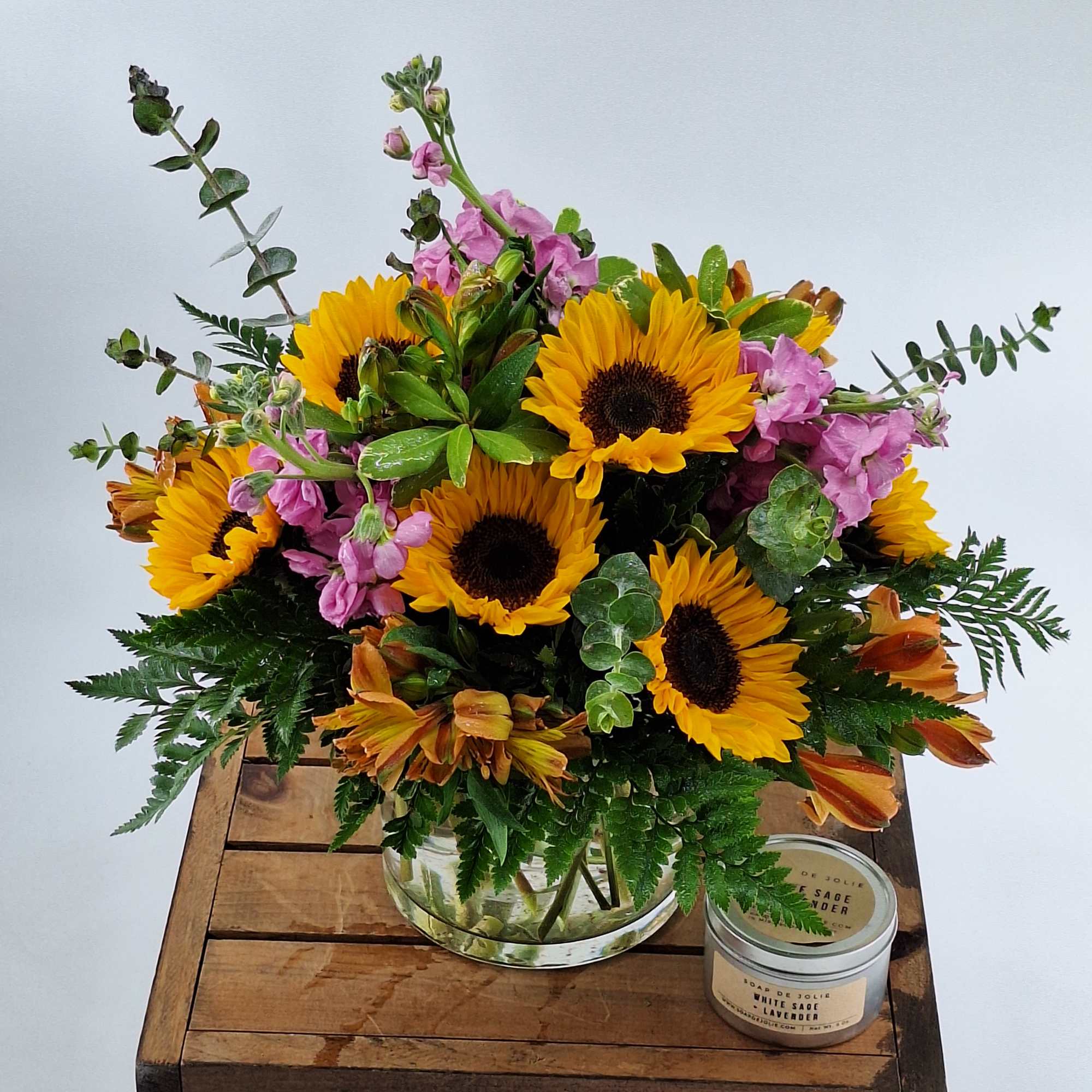 Bouquet of sunflowers and pink stock in a glass vase with a candle beside it.