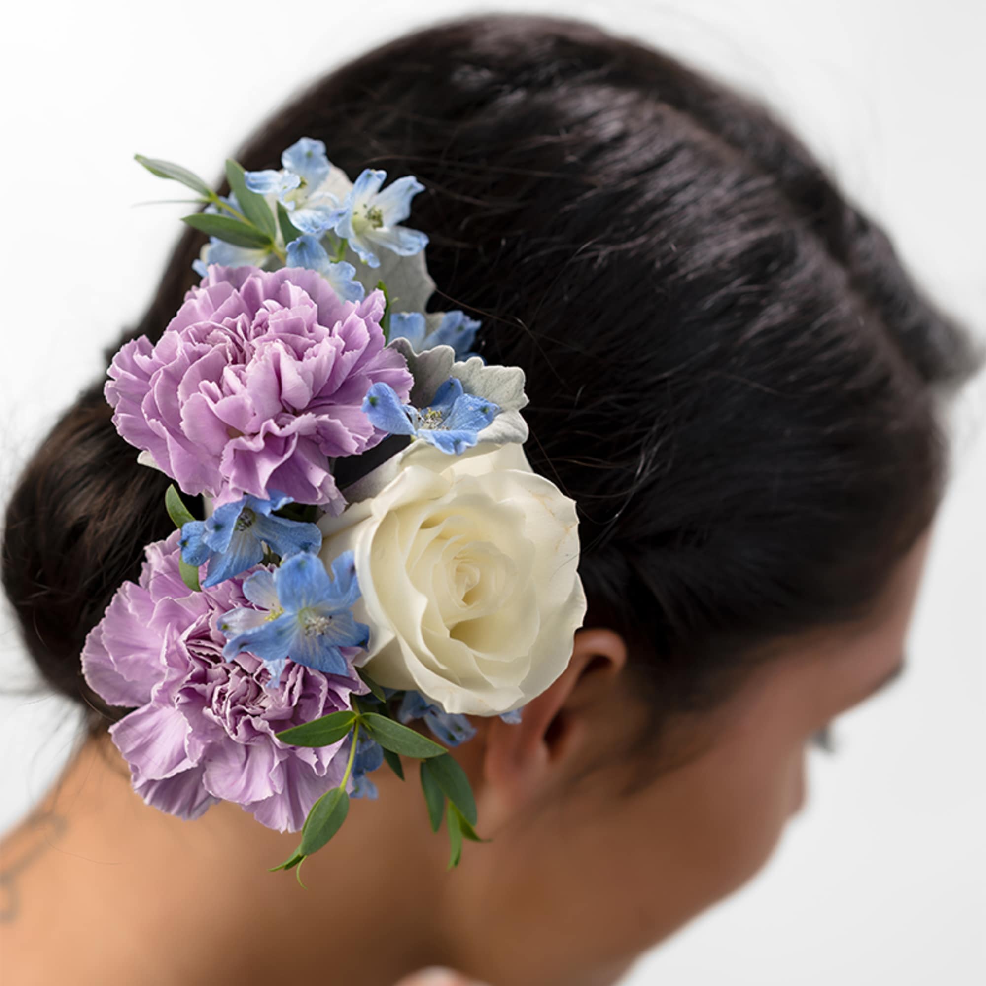Floral hairpiece with lavender carnations, blue delphinium, and a white rose on dark hair.
