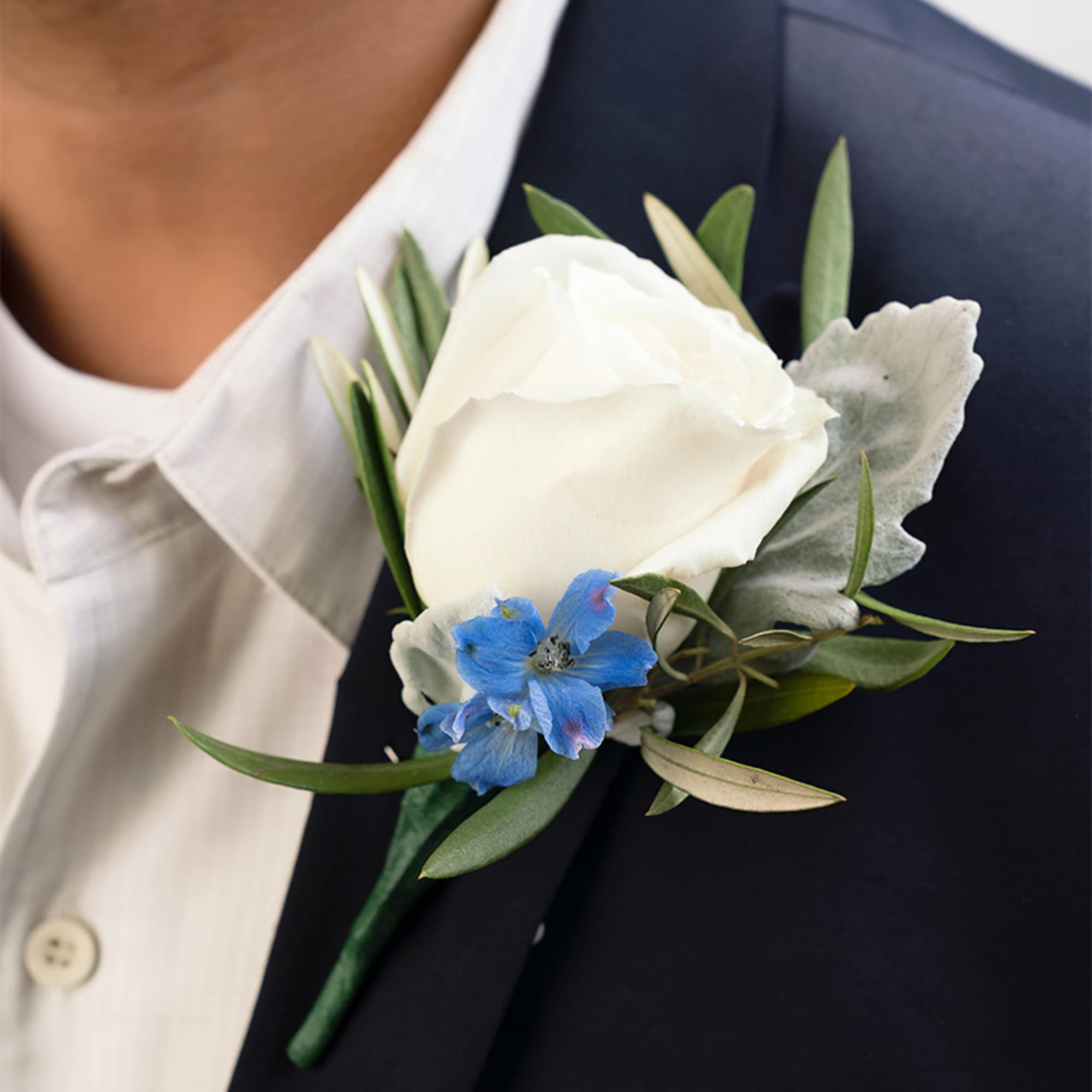 White rose and small blue flower boutonniere pinned to a dark suit jacket