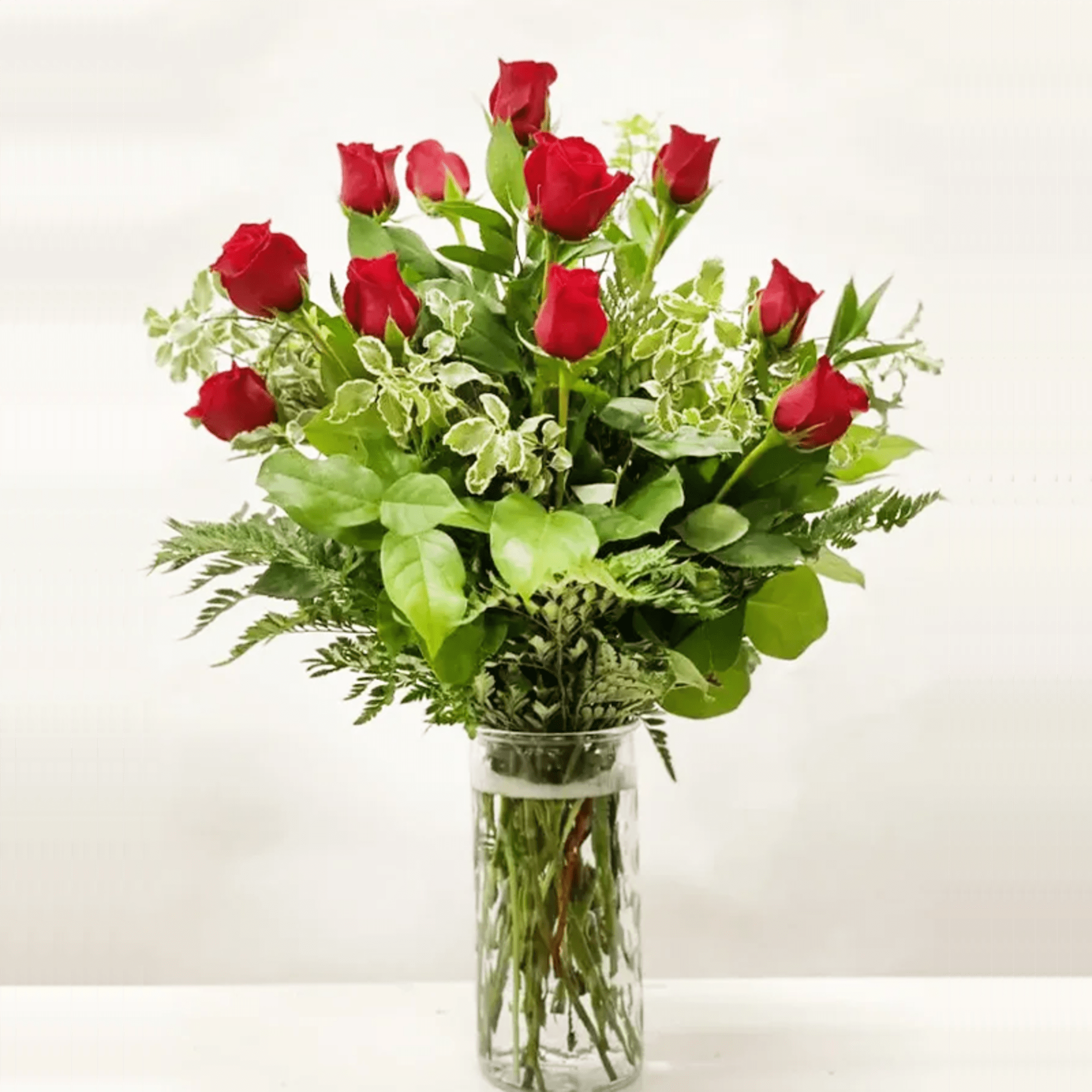 Bouquet of red roses with abundant greenery in a tall clear glass vase
