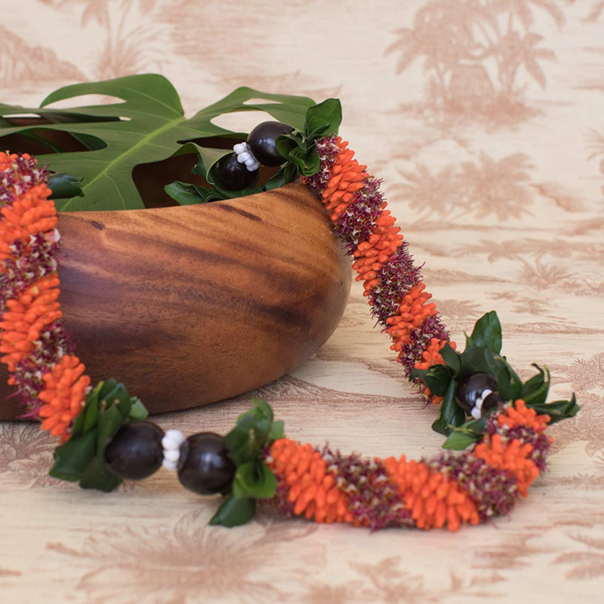 Hawaiian-style lei of orange flowers and dark beads draped beside a wooden bowl