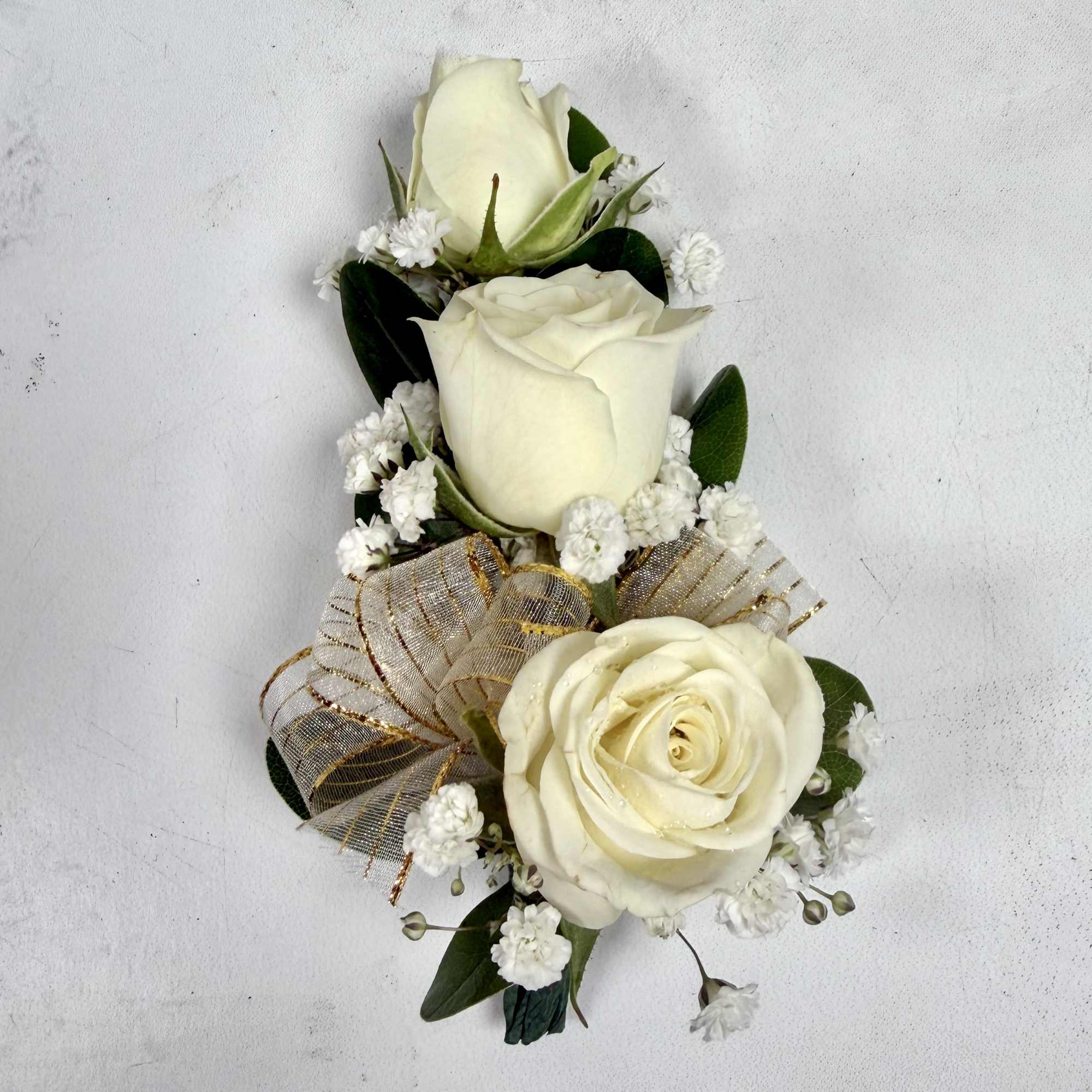 This wrist corsage features three white spray roses, babies breath and white
