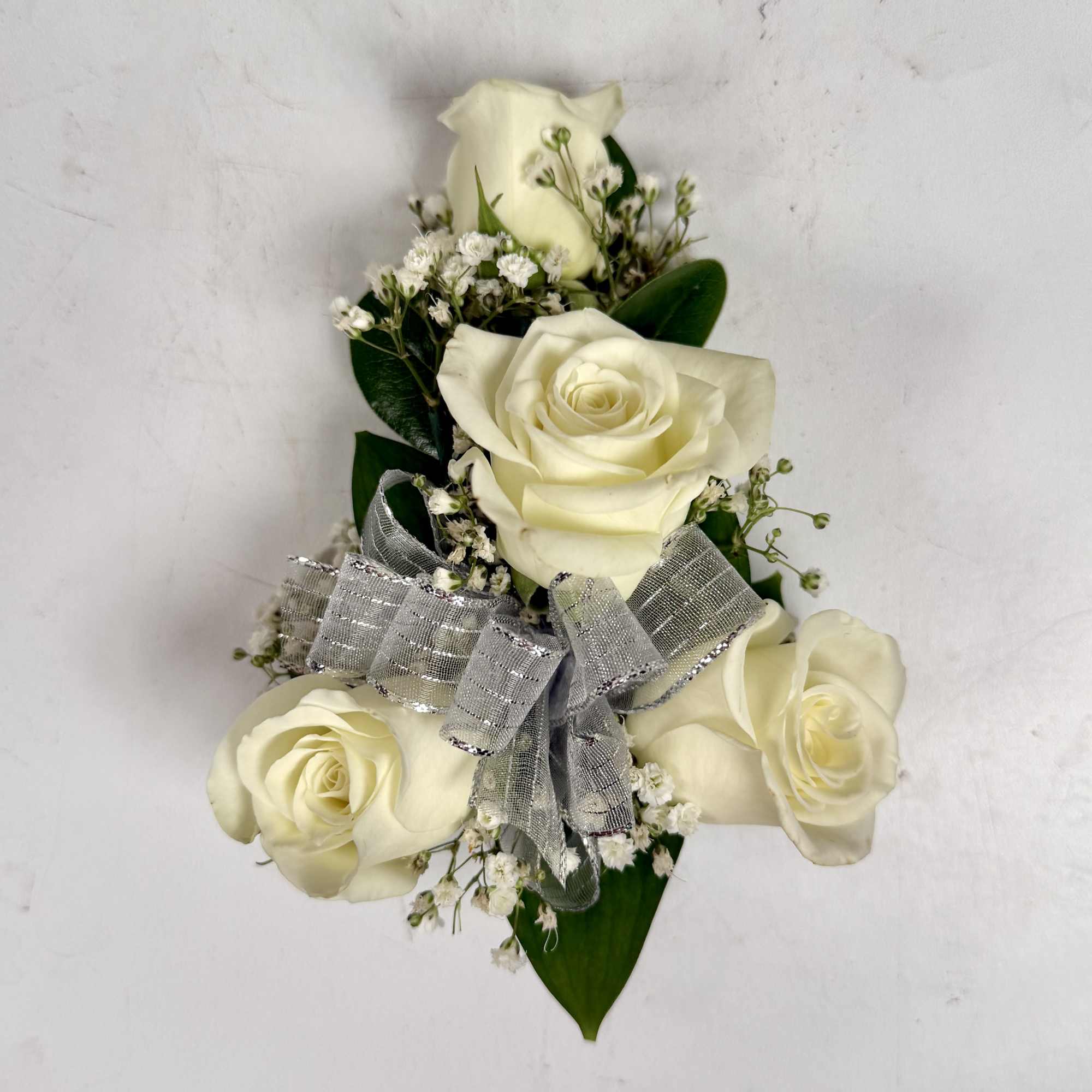 This wrist corsage features three white spray roses, babies breath and white