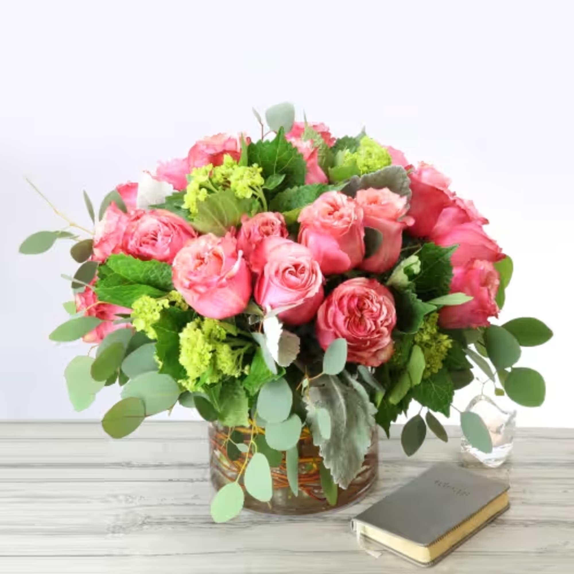 Pink rose bouquet in a glass vase with greenery on a white table