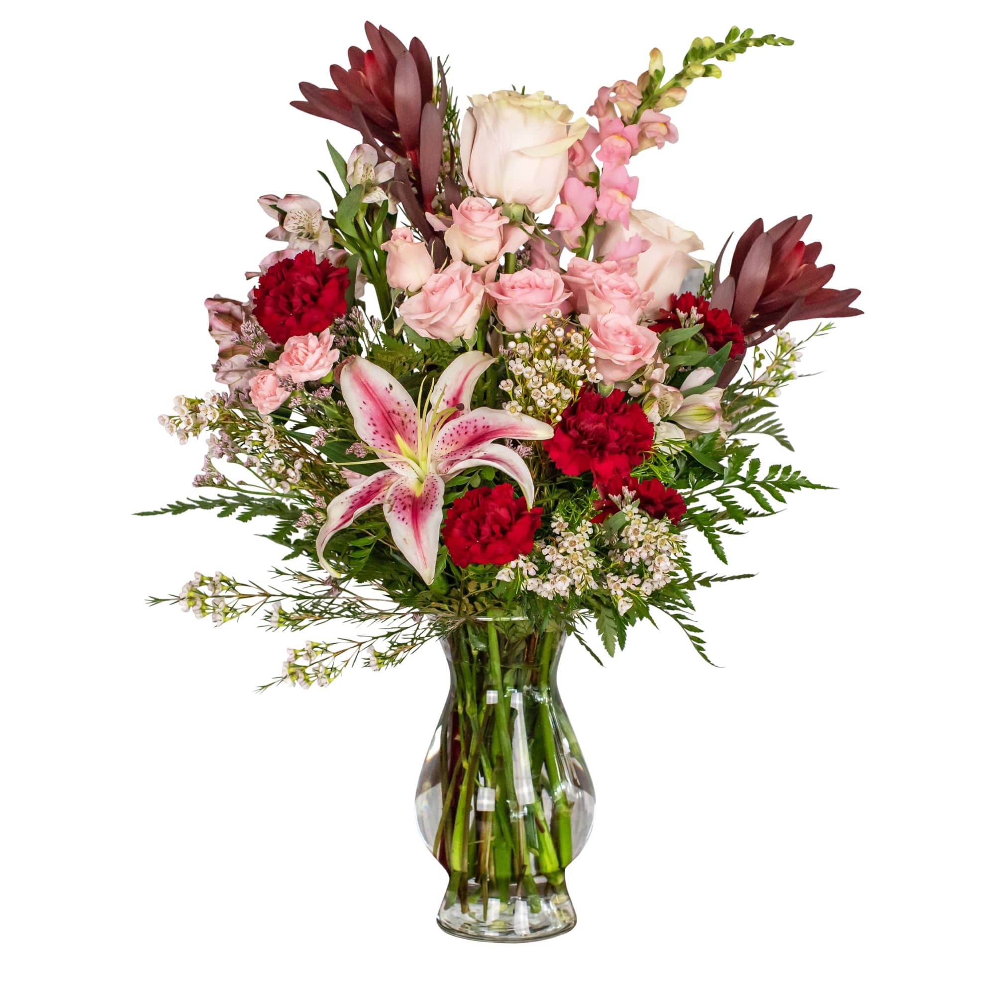 Mixed bouquet of pink roses, red carnations, and a pink lily in a glass vase.