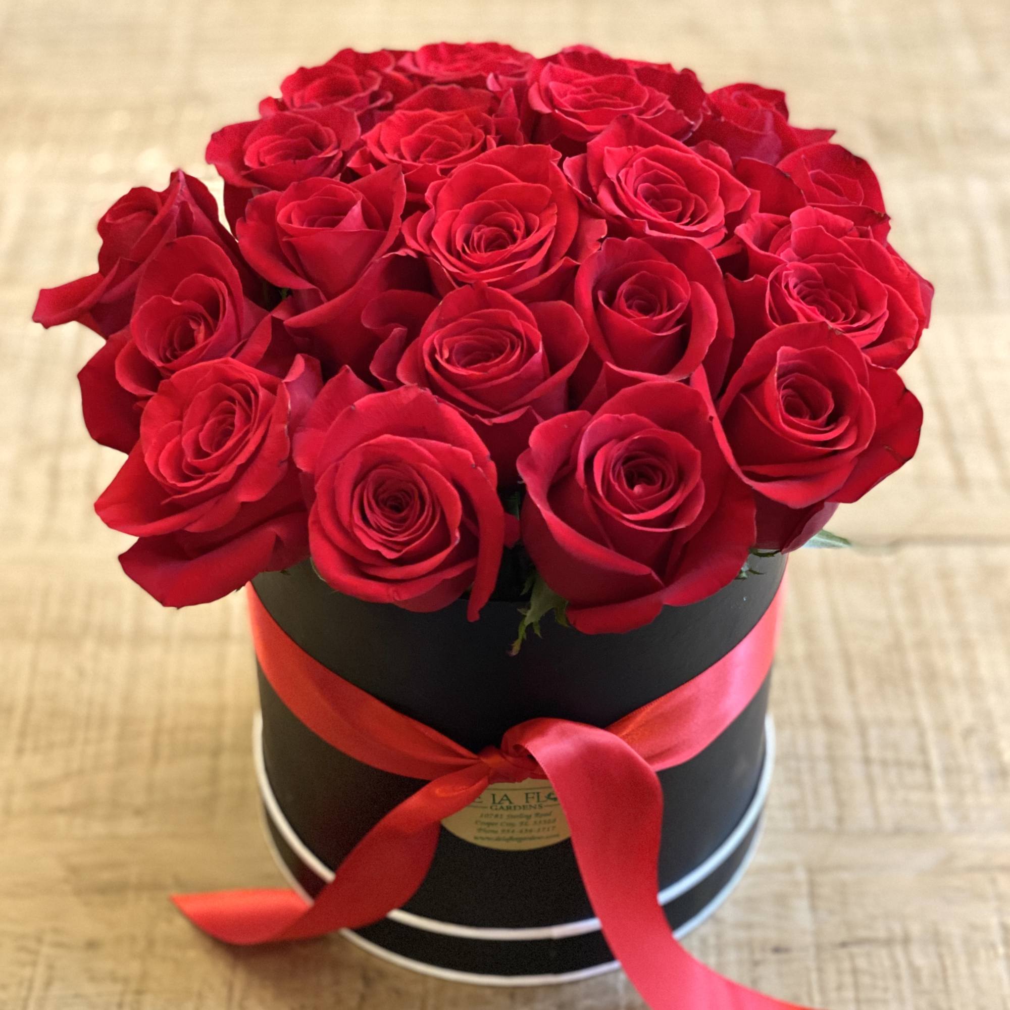 Red roses arranged in a black round box with a red ribbon