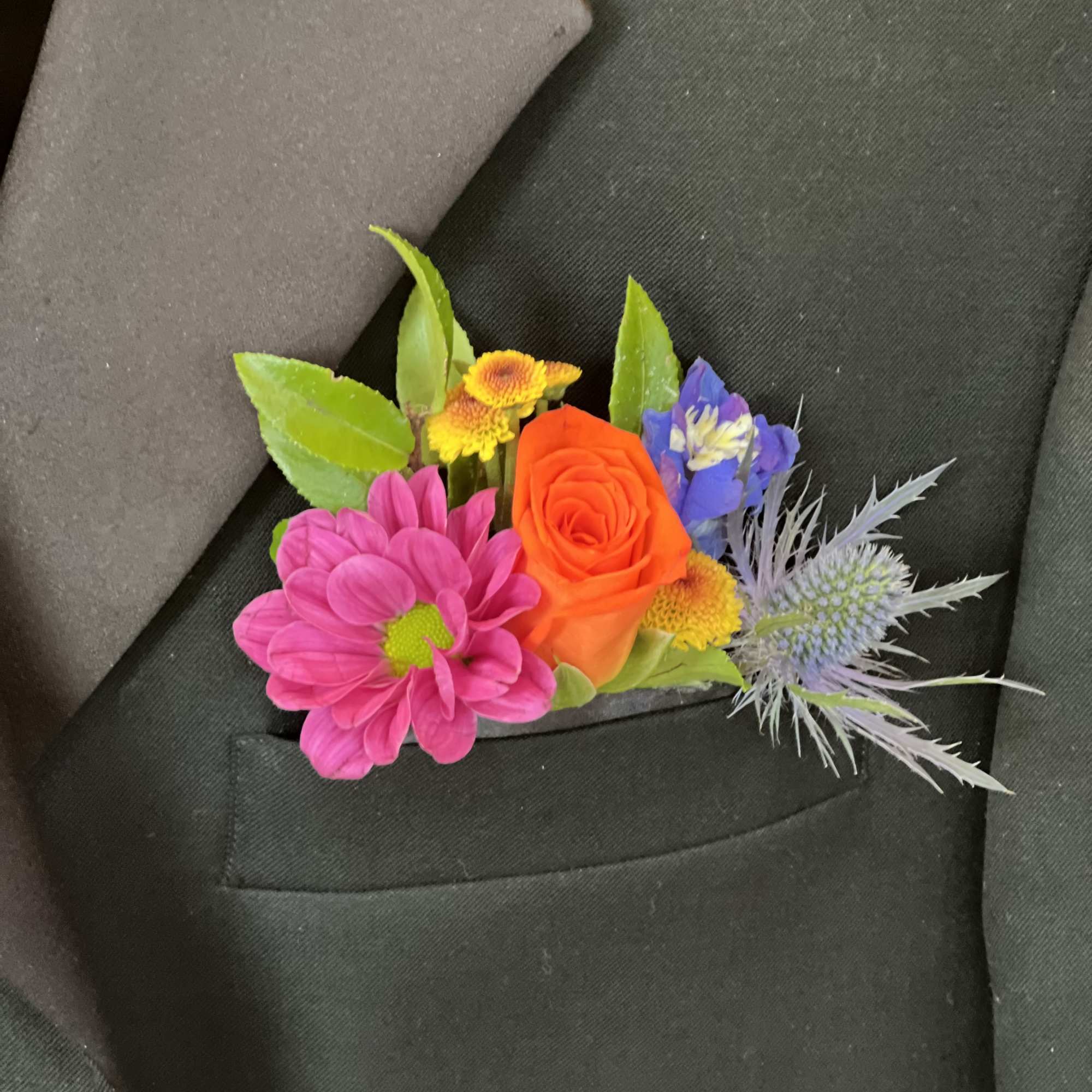Colorful boutonniere with pink daisy, orange rose and mixed blooms in a black suit pocket