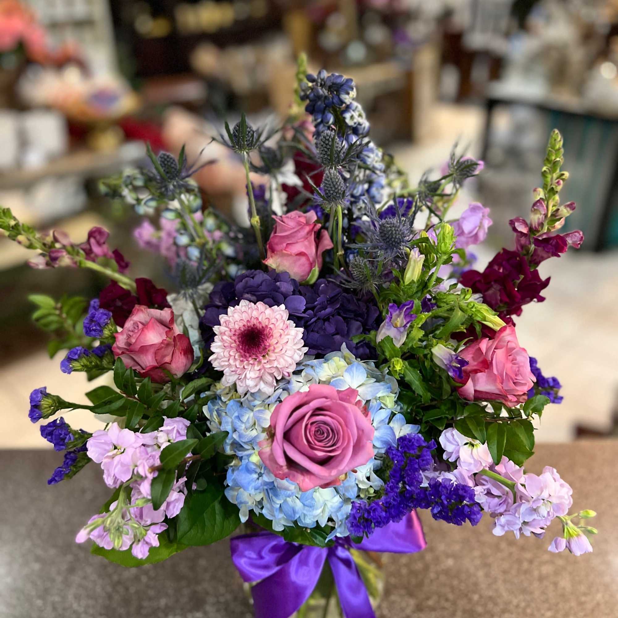 Mixed bouquet of pink and purple flowers in a glass vase with a purple ribbon