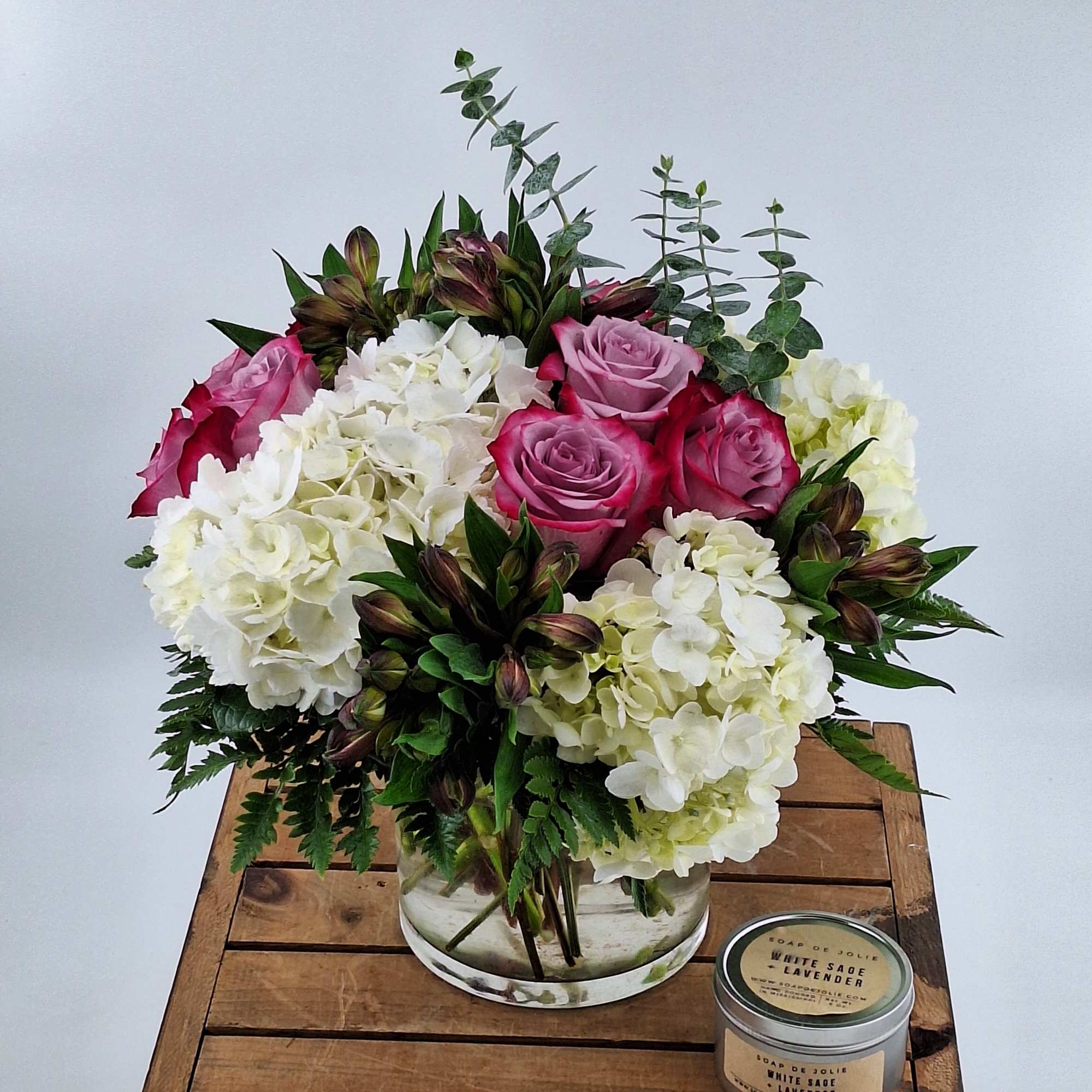 Pink roses and white hydrangeas in a clear glass vase with a candle beside it