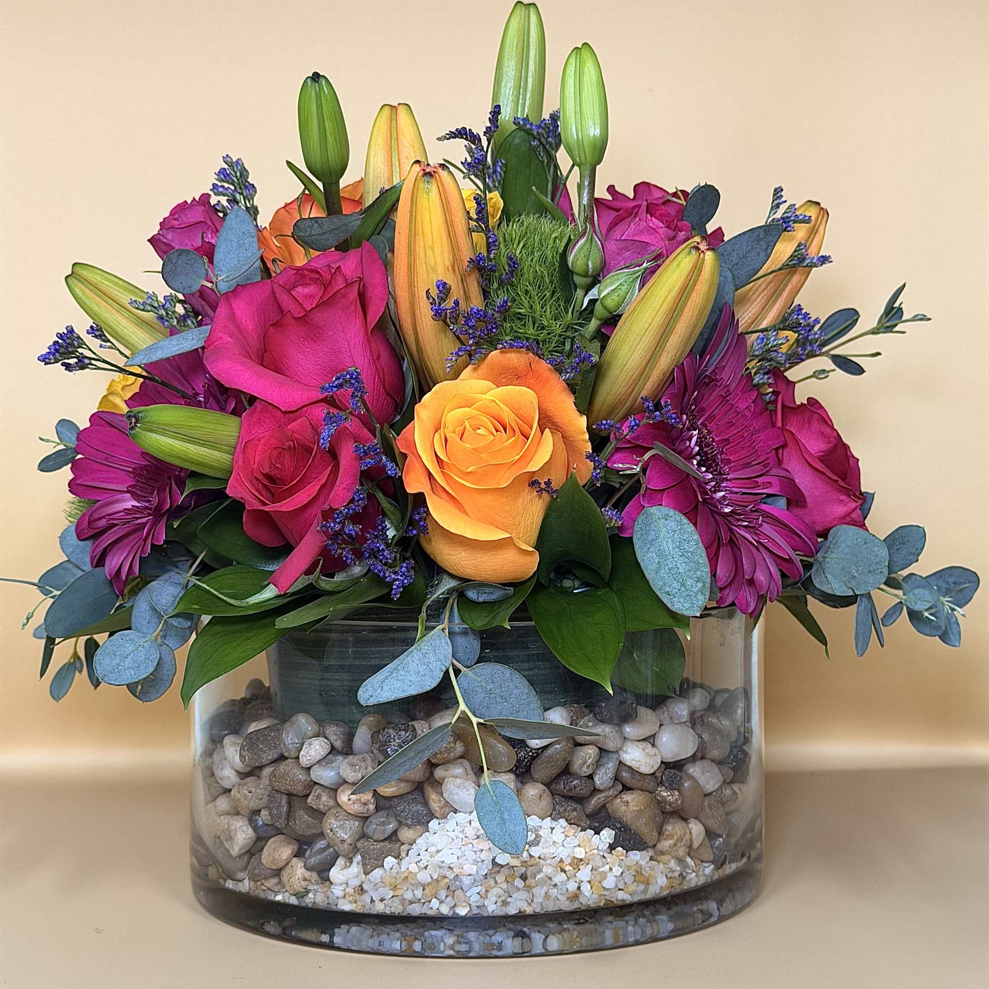 Mixed bouquet of roses and lilies in a glass vase with pebbles