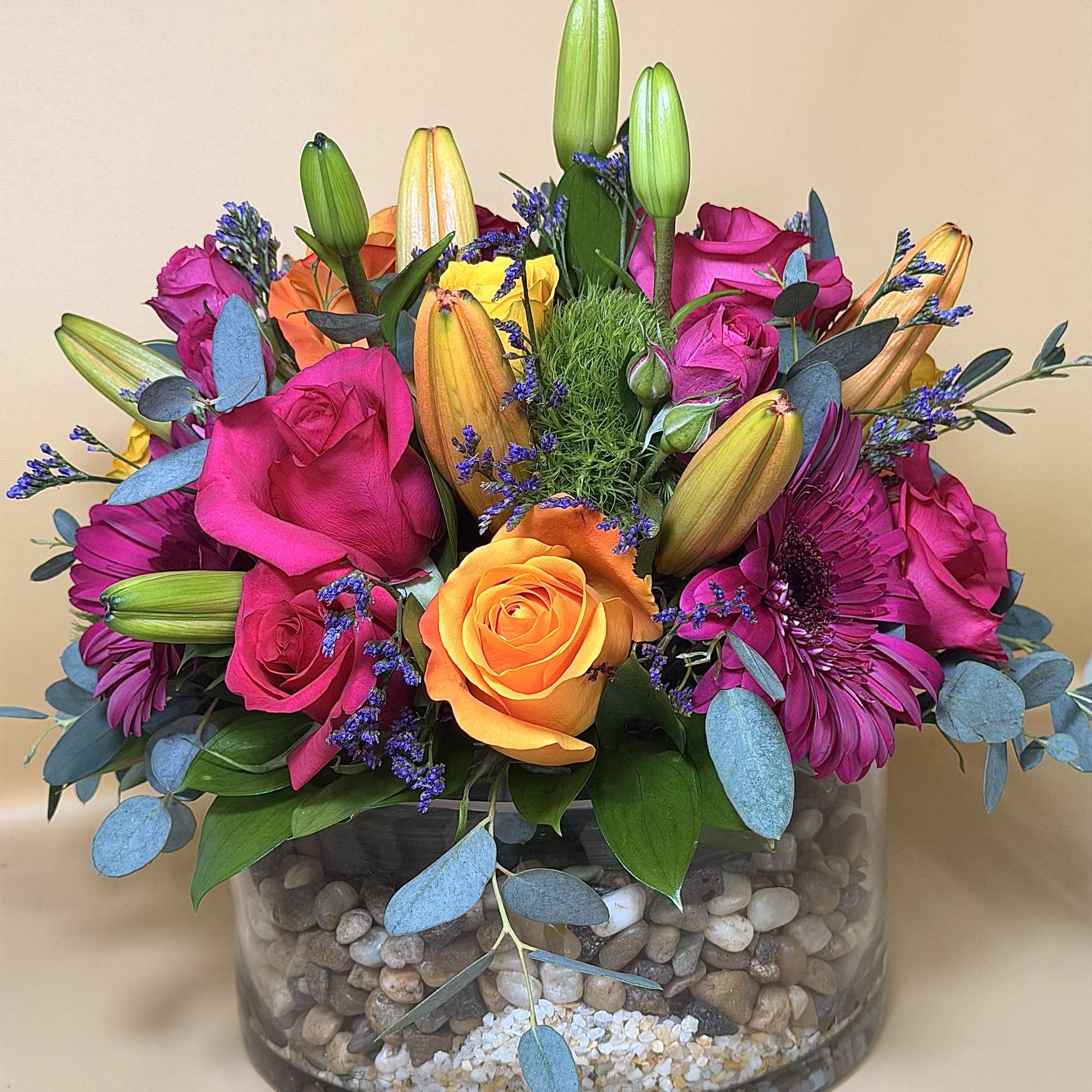 Bright mixed bouquet in a glass bowl vase with roses, lilies, and daisies