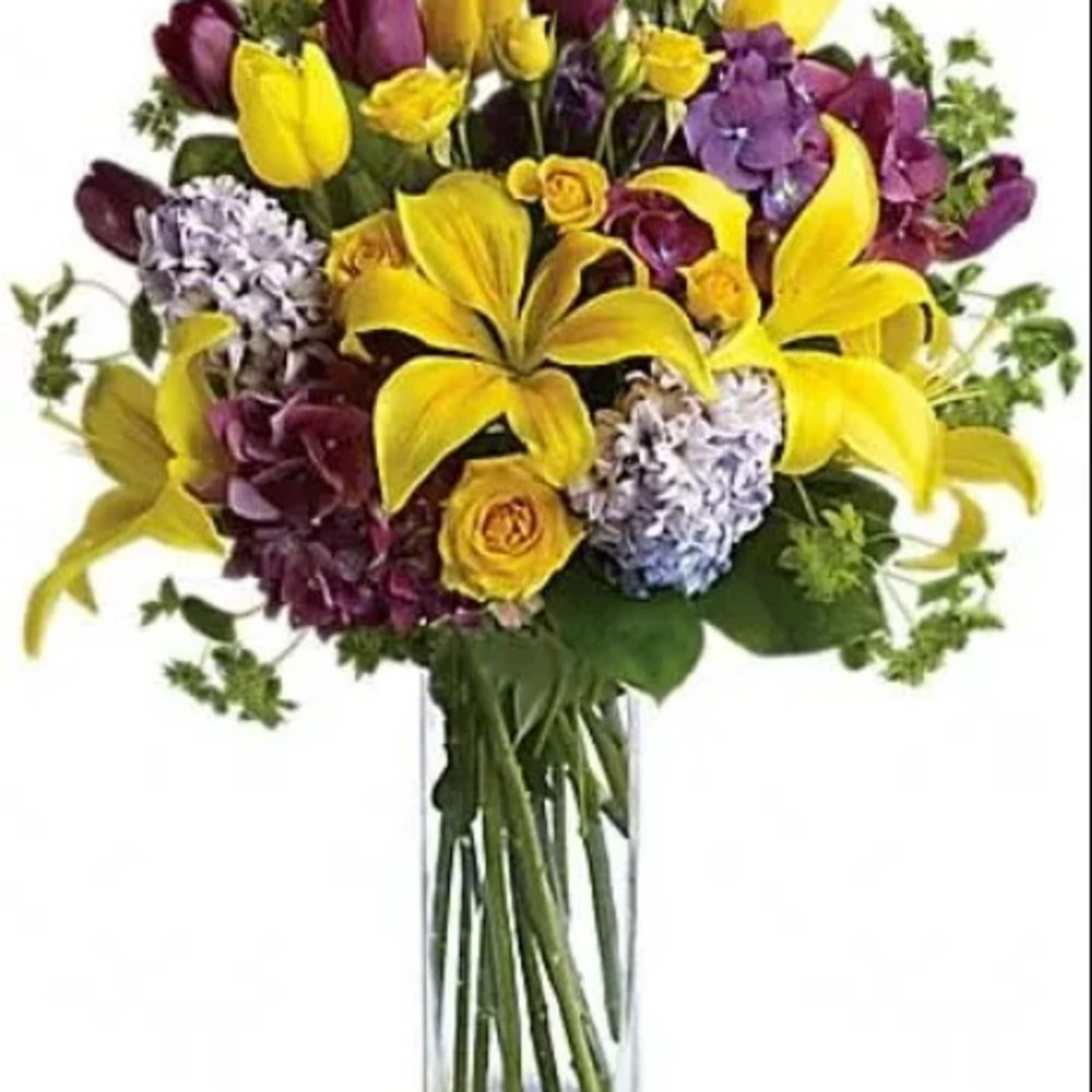 Yellow lilies and purple flowers in a clear glass vase