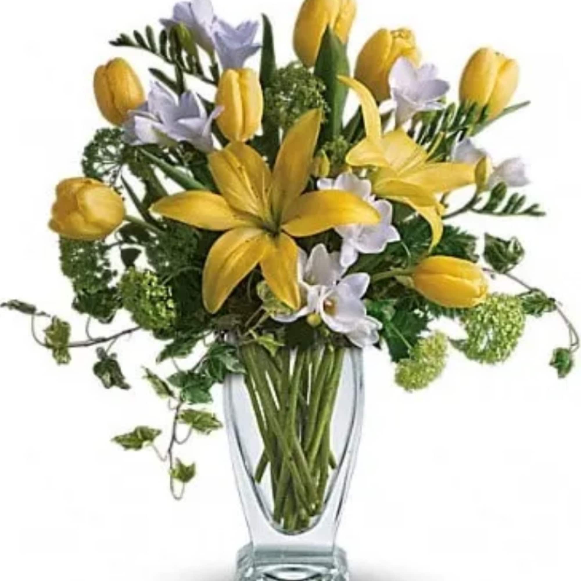 Yellow tulips and pale lavender flowers in a clear glass vase