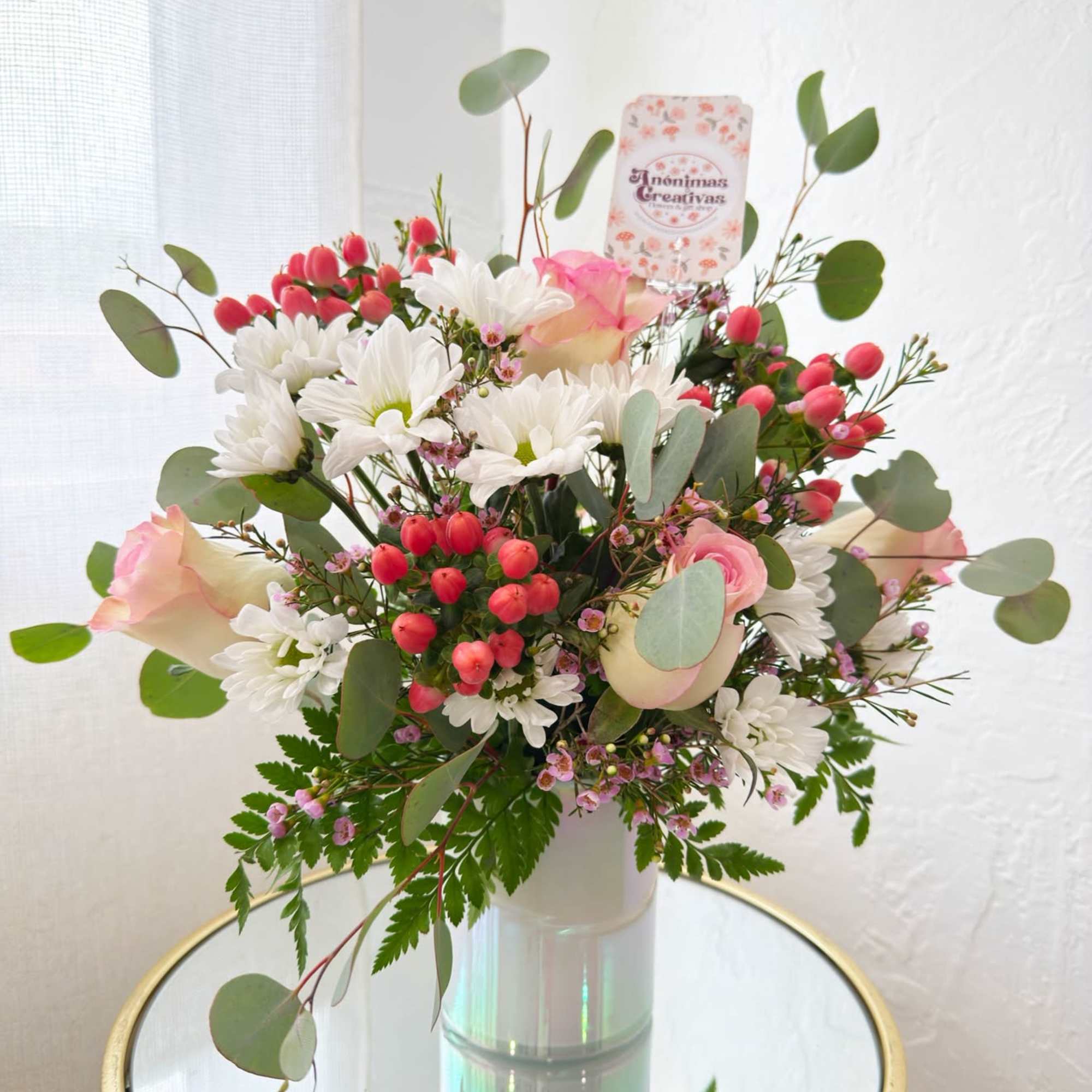 Bouquet of white daisies, pink roses, and red berries in a glass vase