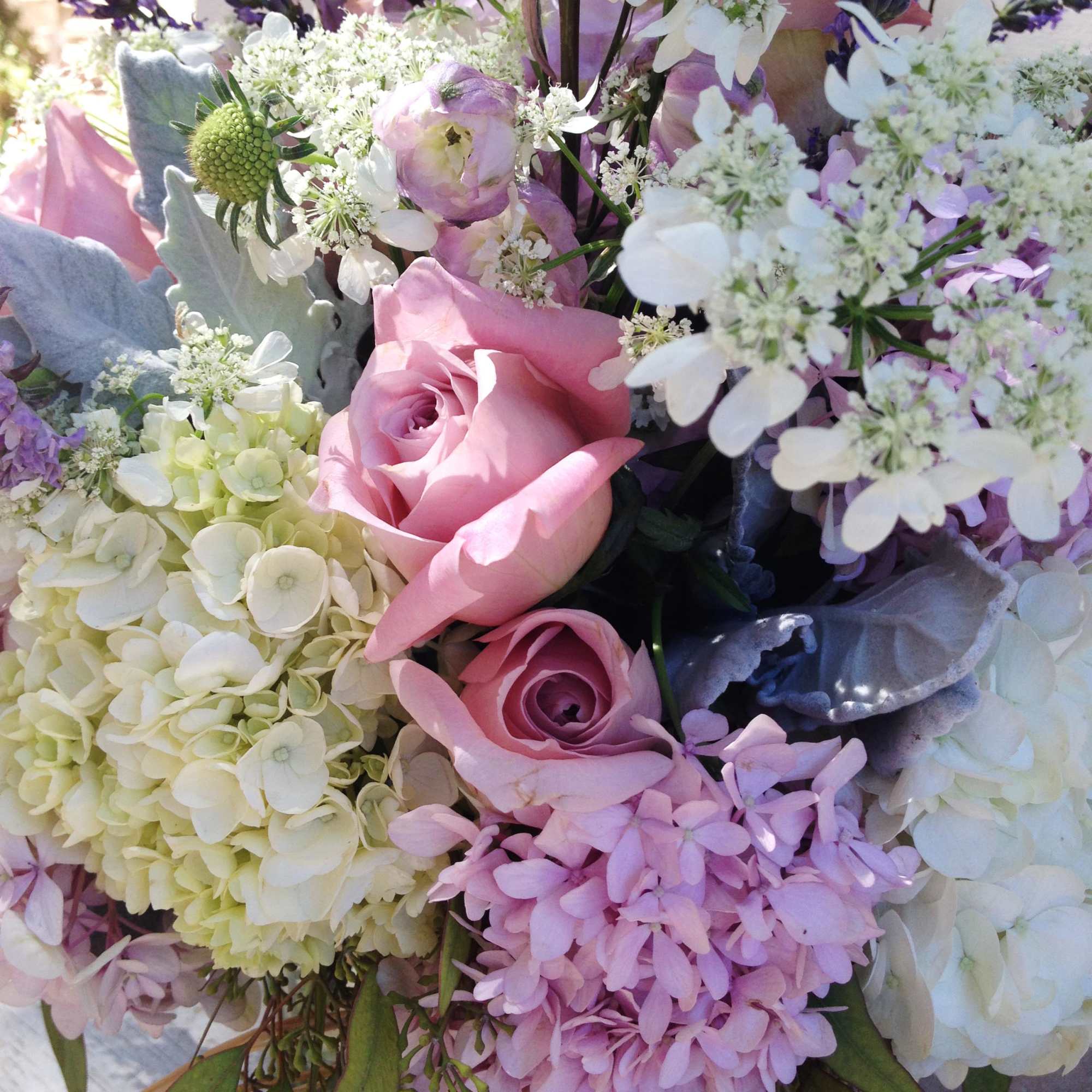 Pastel arrangement of pink roses, hydrangeas, lisianthus and white filler flowers in a clear glass vase.