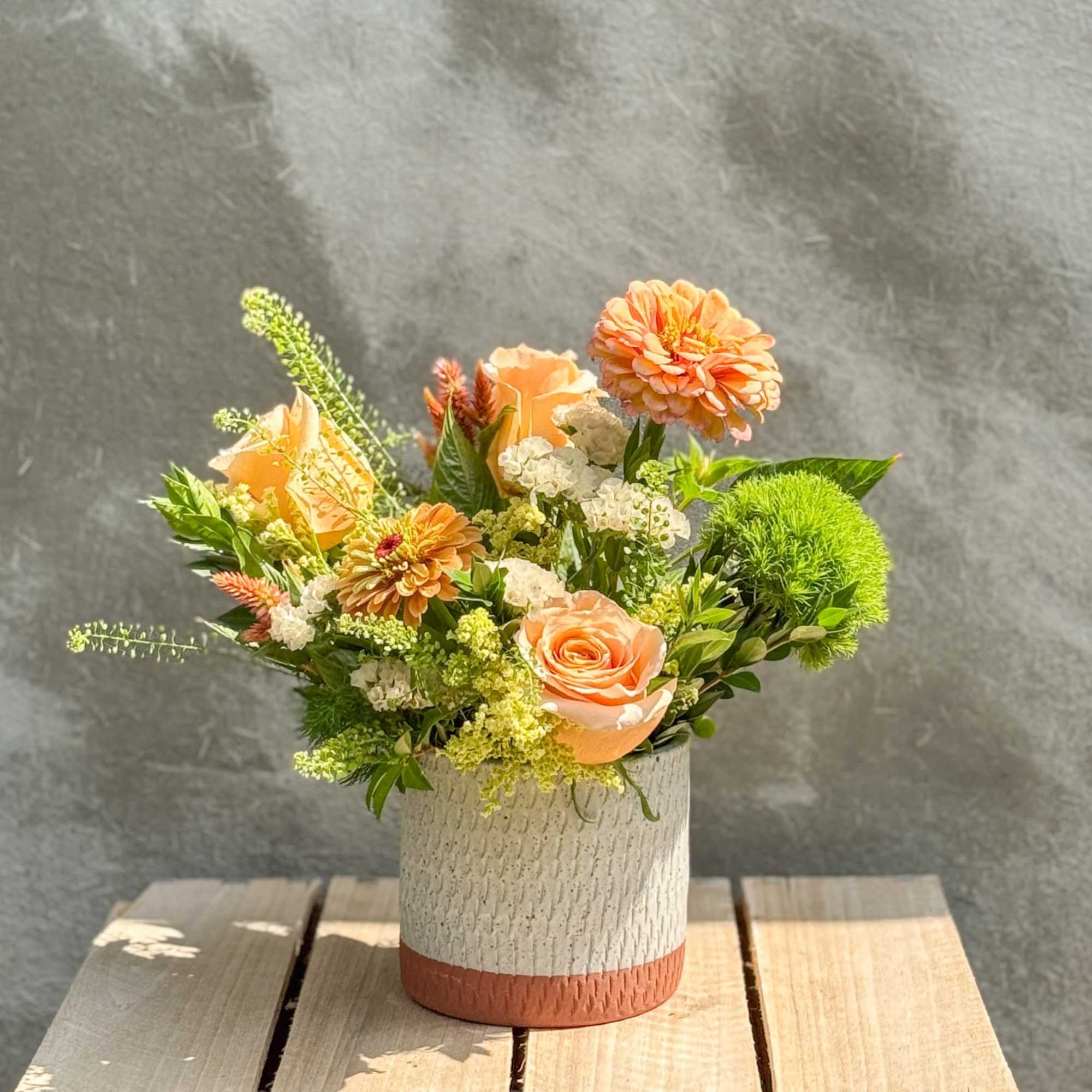 Peach roses and mixed flowers in a white and terracotta ceramic pot on a wooden table